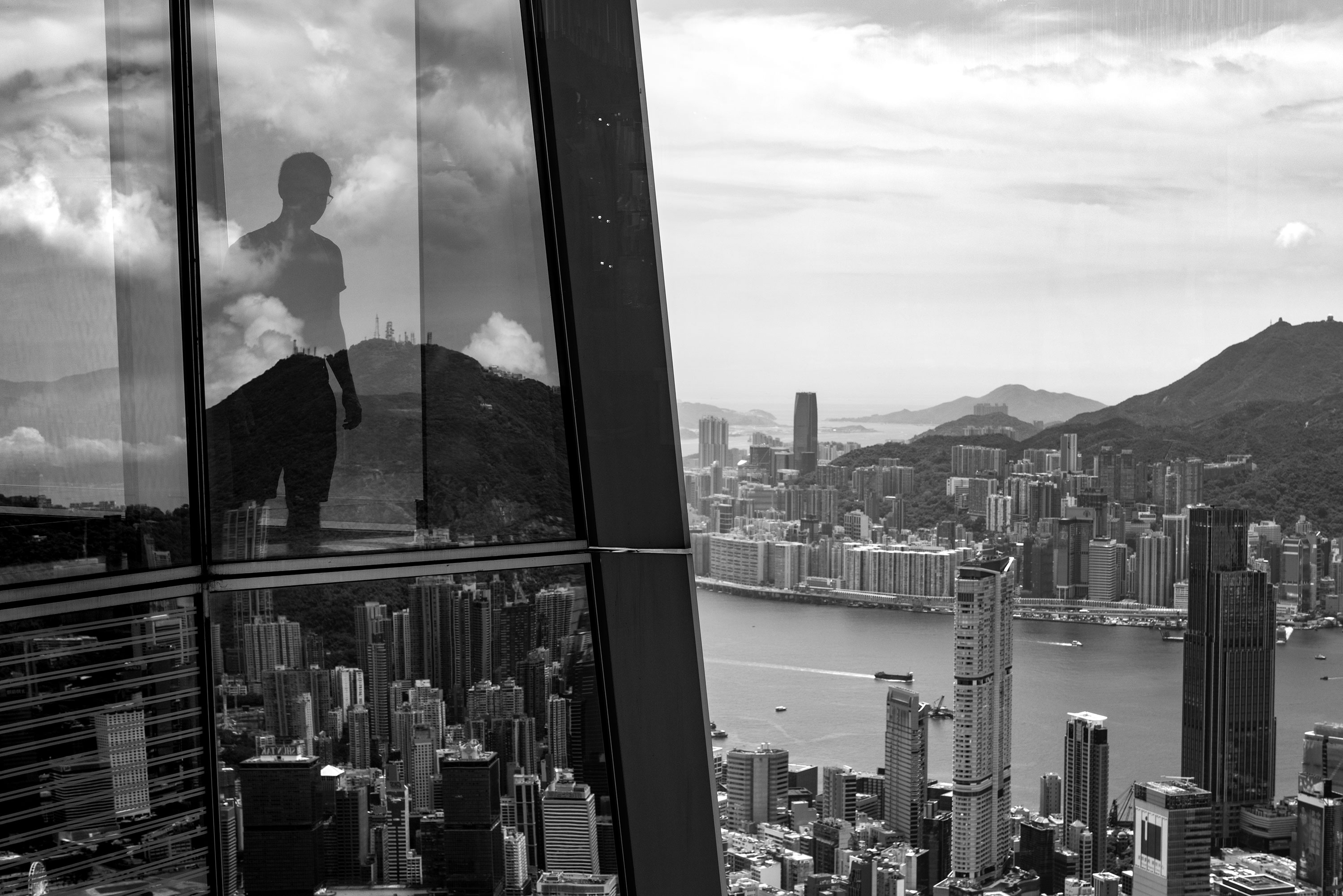 Black and white photography of a person looking down the street from the 100th of the highest tower in Kowloon taken by Jennifer Esseiva.