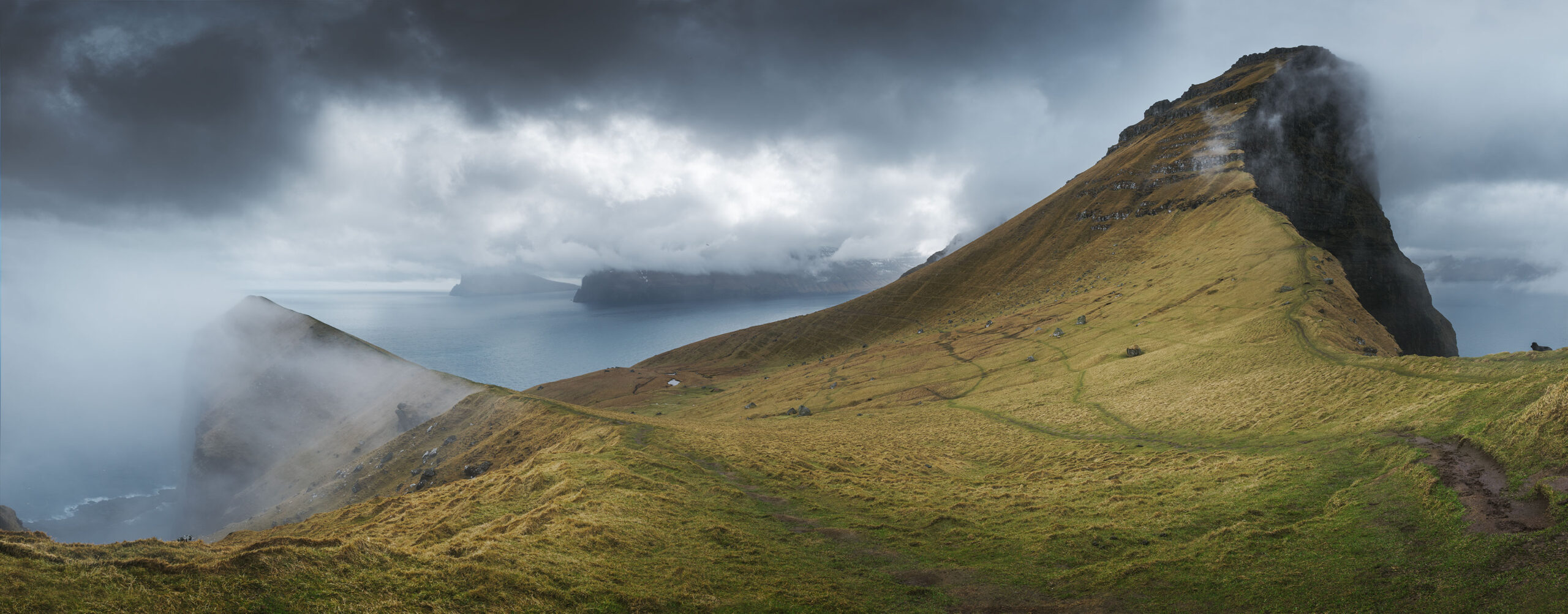 Panorama of the island of Kalsoy and the Kallur Lighthouse under a dark and dramatic sky.