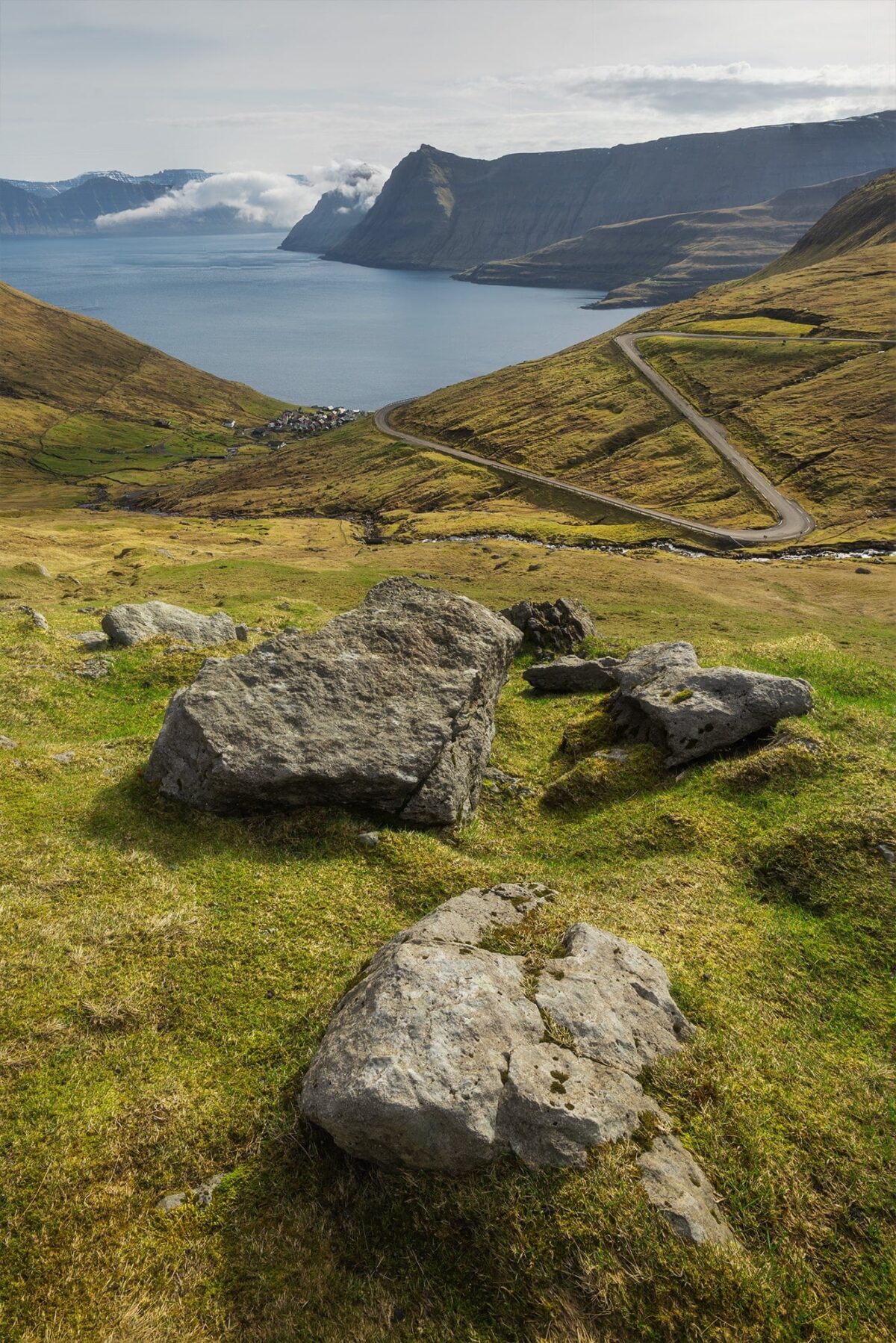 Winding road above Funningur village, Faroe Islands, with fjord and dramatic mountains under soft light