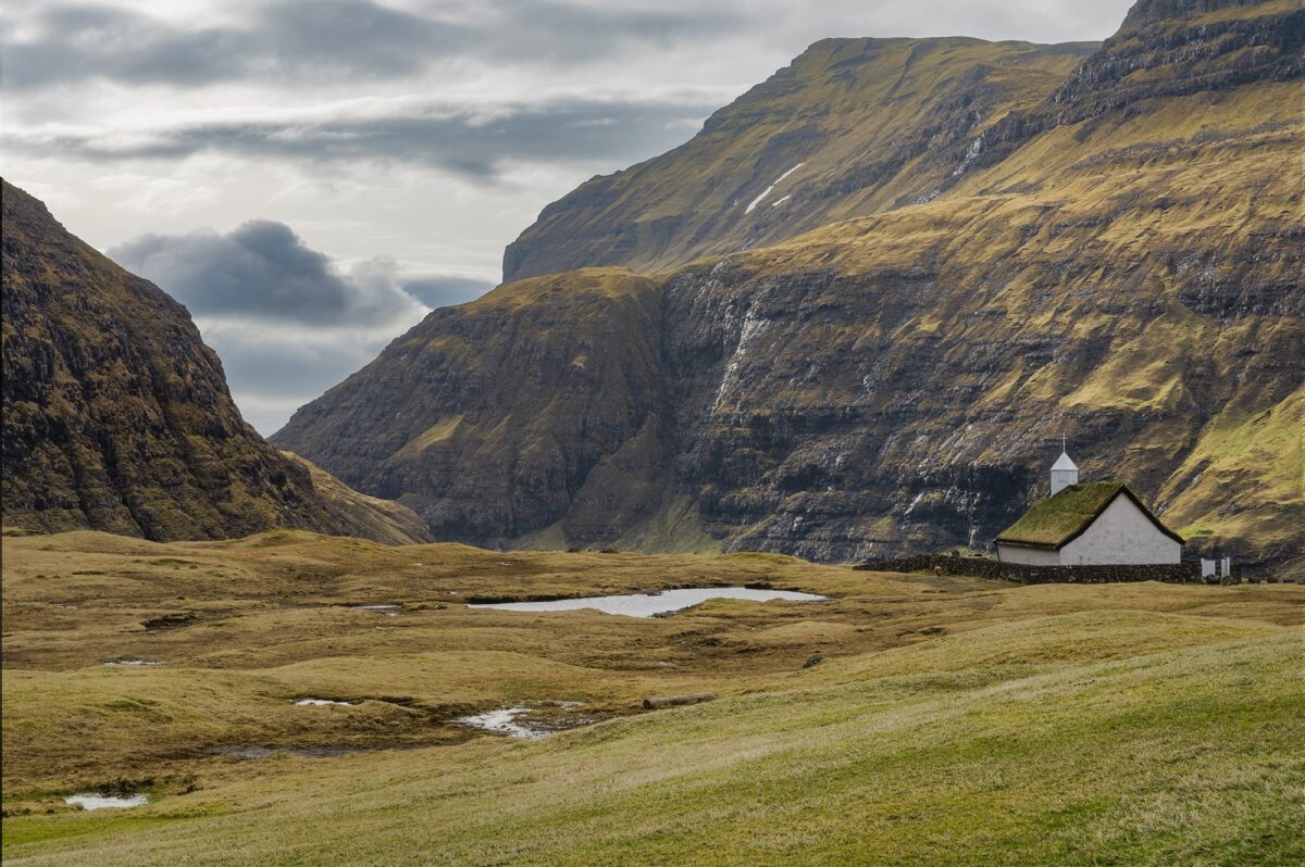 Saksun church with grass roof surrounded by mountains and soft light, Faroe Islands.