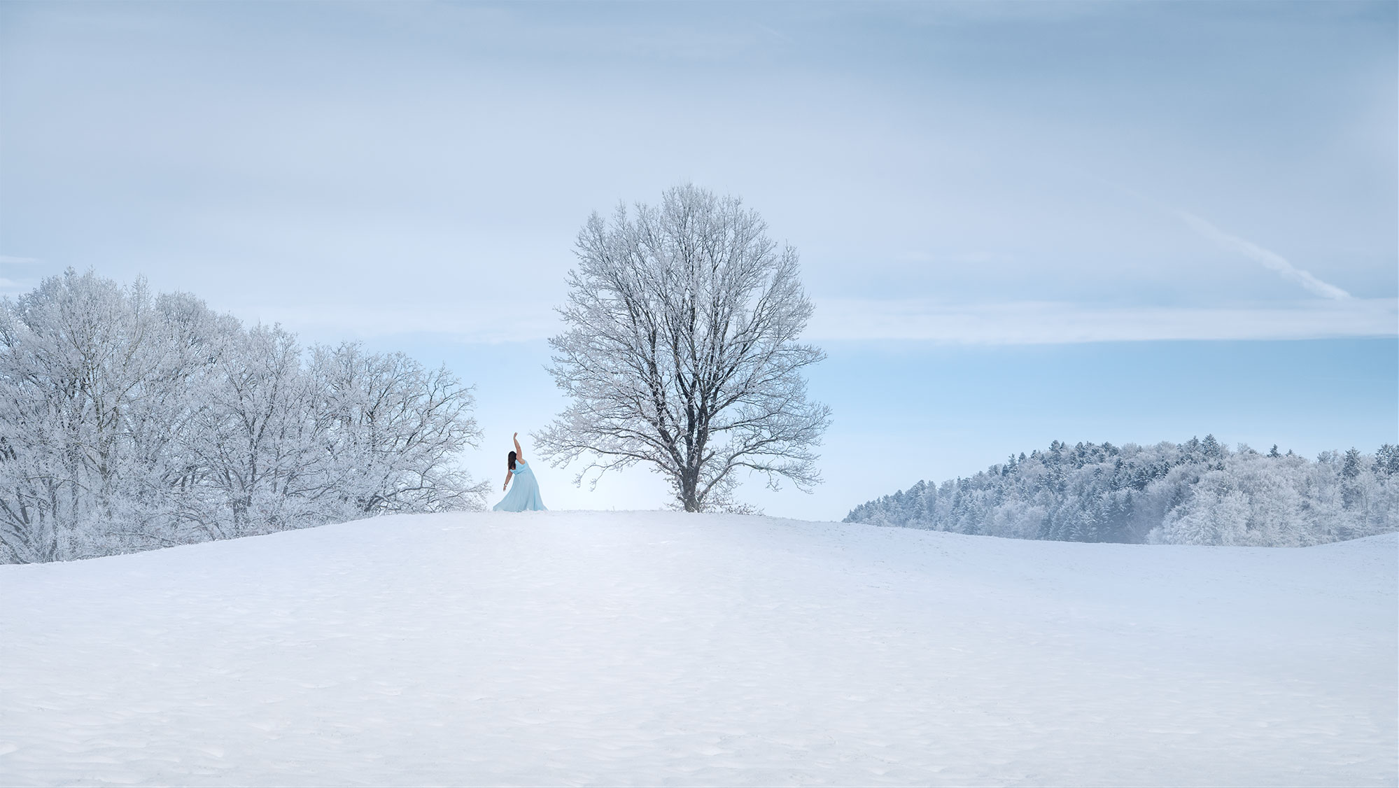 Immerse yourself in the captivating world of Swiss landscape photographer Jennifer Esseiva with this autoportrait. Adorned in a flowing ice-blue dress, she celebrates body positivity against the serene snowy backdrop of Canton Fribourg. Witness the magic of a lone frost-covered tree, standing as a symbol of resilience and beauty in the wintry countryside.