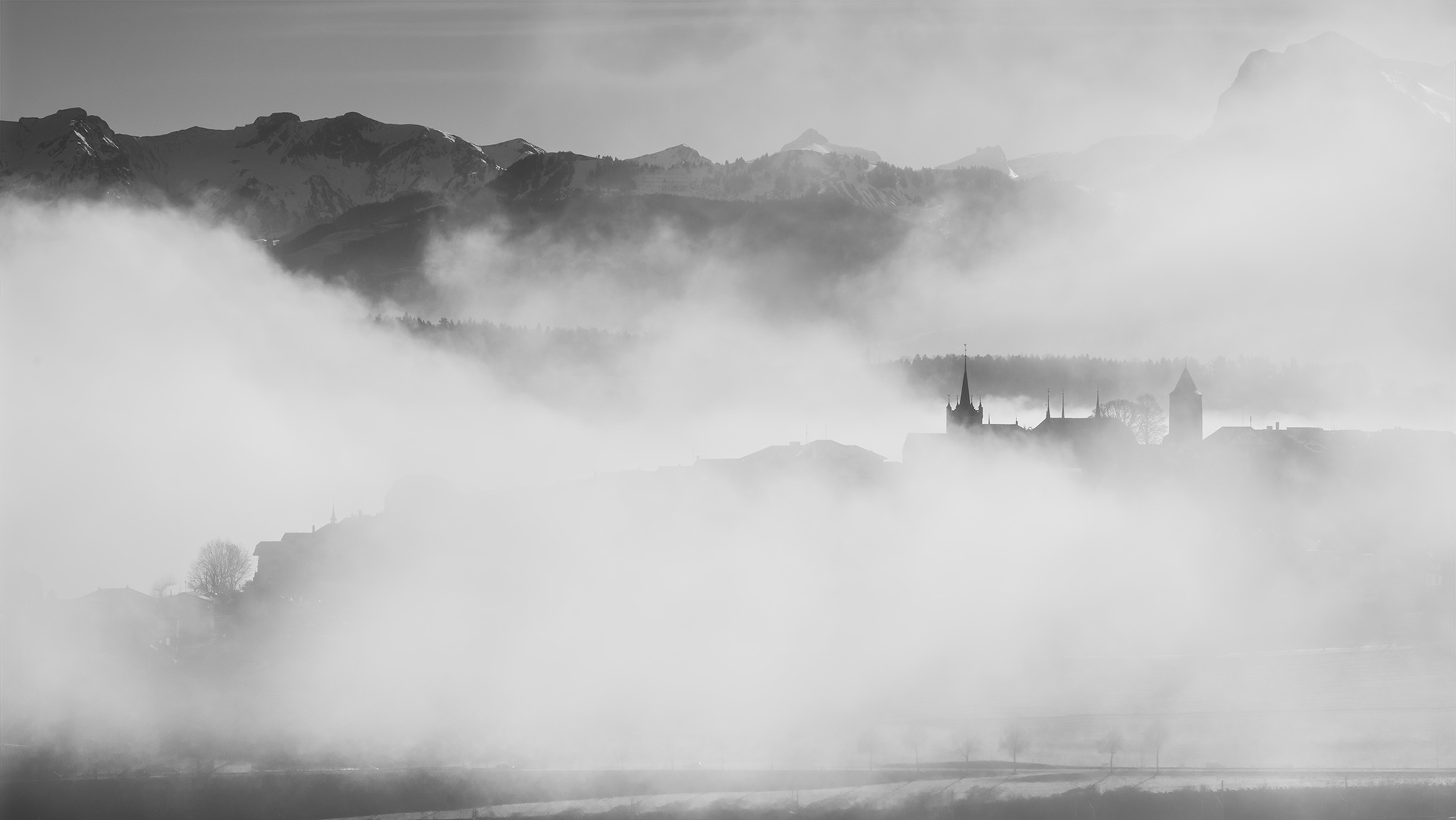 Swiss artist Jennifer Esseiva, wielding her Nikon Z8, presents a captivating black and white landscape photograph capturing the city of Romont in the fog. This mesmerizing scene unfolds in the countryside of Canton Fribourg, Switzerland. Explore the subtle beauty of the mist-shrouded landscape through Jennifer's lens.