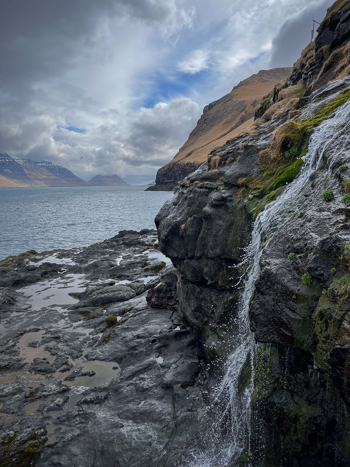 This serene image captures the tranquil beauty of a small waterfall on Kalsoy Island.