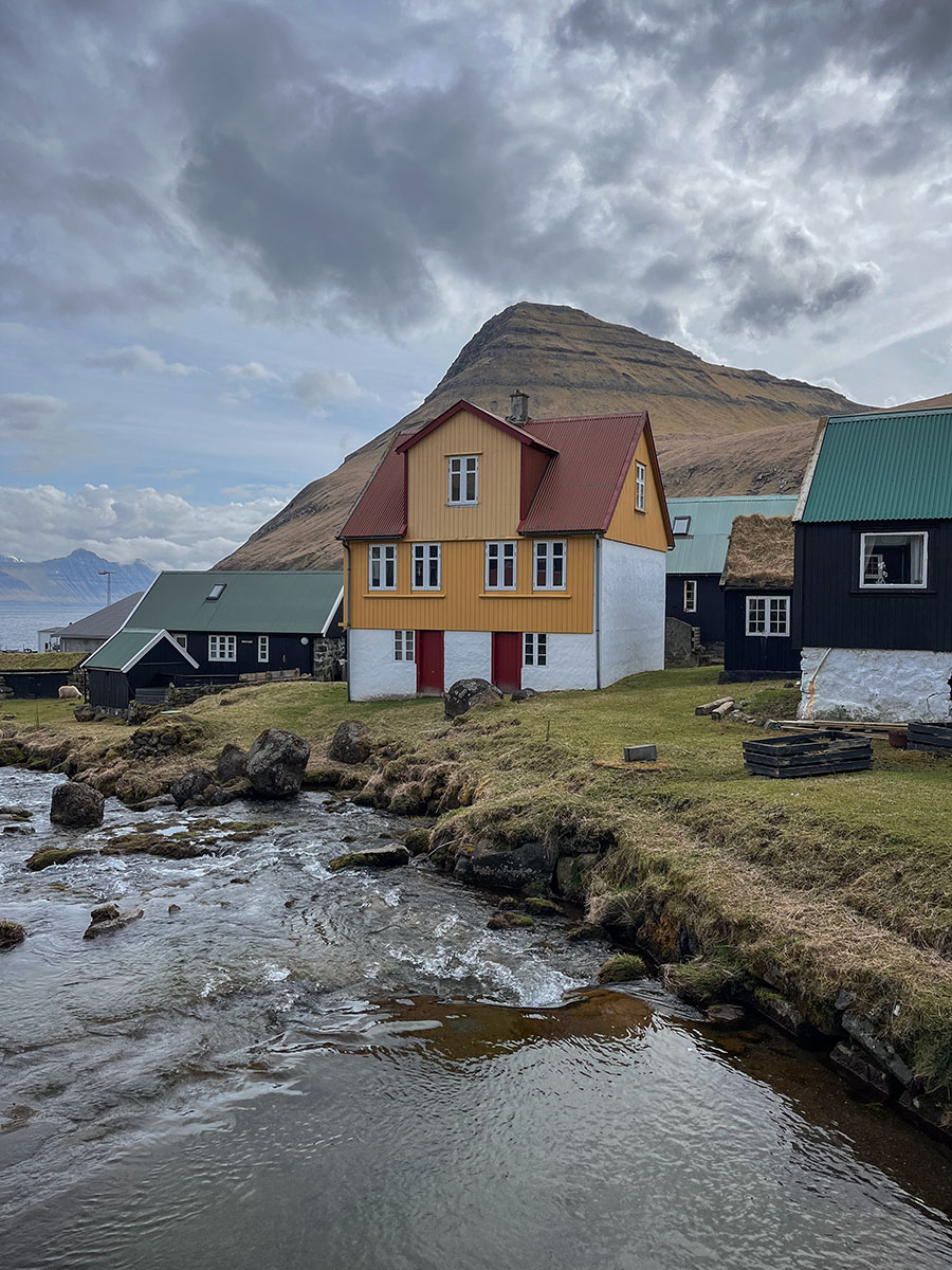 This landscape photograph captures the picturesque charm of Gjógv village in the Faroe Islands, featuring its iconic yellow house as a focal point.