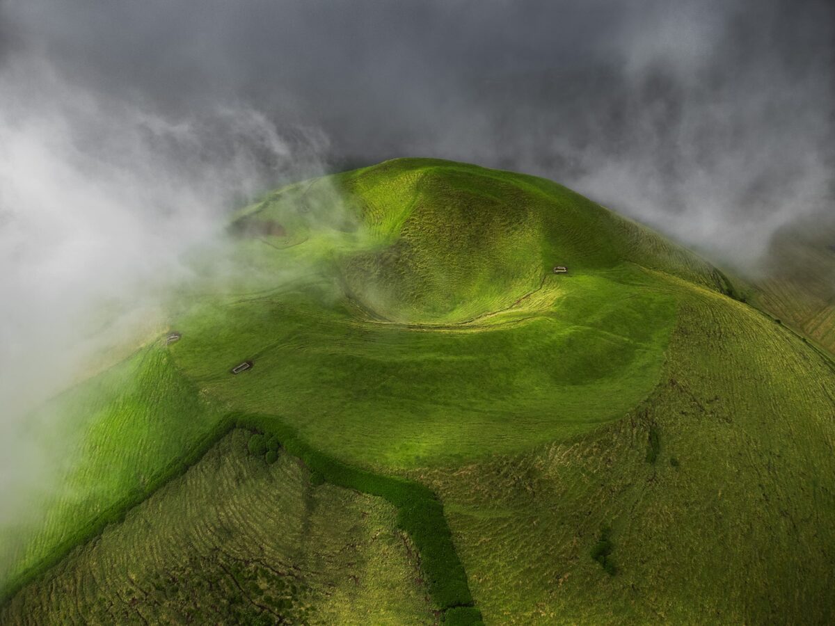 Aerial drone landscape photography of Pico Island, Azores, showing lush green terrain and the silhouette of Mount Pico rising above the volcanic plateau.