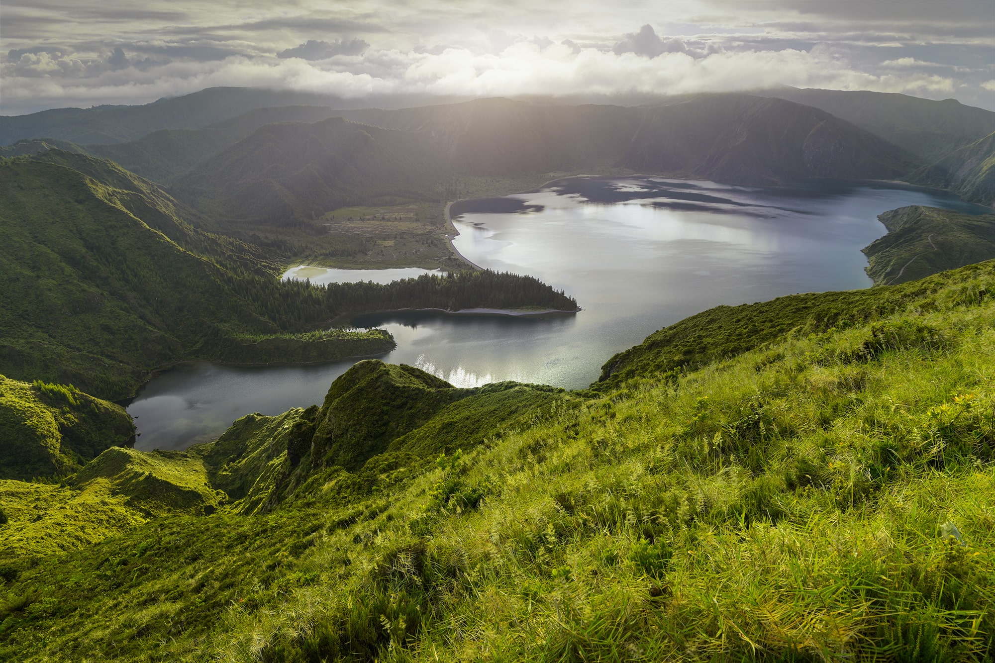 Enter the realm of enchantment with this captivating landscape photograph taken by Jennifer Esseiva using her Nikon D810. At Lake Fogo in Sao Miguel, the dawn breaks with a spectacle of light, as rays pierce through the clouds, casting an ethereal glow upon the serene waters below. This mystical landscape invites viewers to immerse themselves in the magical beauty of Sao Miguel, where nature's wonder unfolds with each passing moment. Esseiva's expert composition and keen eye for detail capture the essence of this captivating scene, evoking a sense of tranquility and awe. Join Esseiva on this visual journey through the mystical landscapes of Sao Miguel, where every frame tells a story of the island's timeless charm and breathtaking vistas.