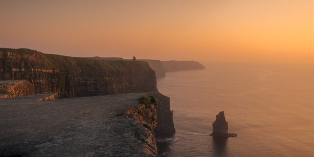 Immerse yourself in the captivating beauty of the Cliffs of Moher in County Clare, Ireland, as the sun sets on the horizon. This stunning landscape photography, captured by Swiss photographer Jennifer Esseiva and her Nikon D810, offers a wide-angle view of the majestic cliffs. Marvel at the rugged coastline, where the cliffs rise dramatically from the crashing waves below, creating a scene of unparalleled natural beauty. Join Jennifer Esseiva on this visual journey as she captures the timeless allure of one of Ireland's most iconic landmarks.