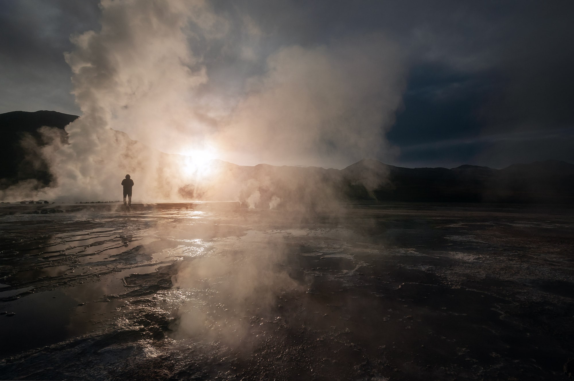 Experience the enchanting spectacle of sunrise casting its radiant rays through the ethereal smoke of the Tatio Geysers in Chile, near San Pedro de Atacama, as captured by acclaimed Swiss artist Jennifer Esseiva using her Nikon D300 camera. This mesmerizing photograph beautifully encapsulates the mystical ambiance of the Tatio Geysers, showcasing nature's symphony of light and steam. Esseiva's expert lenswork captures the magical convergence of dawn and geothermal wonders, transporting viewers to the heart of this otherworldly landscape. Immerse yourself in the artistry of Esseiva's composition, celebrating the interplay of sunlight and geothermal smoke at one of Chile's most captivating natural wonders.