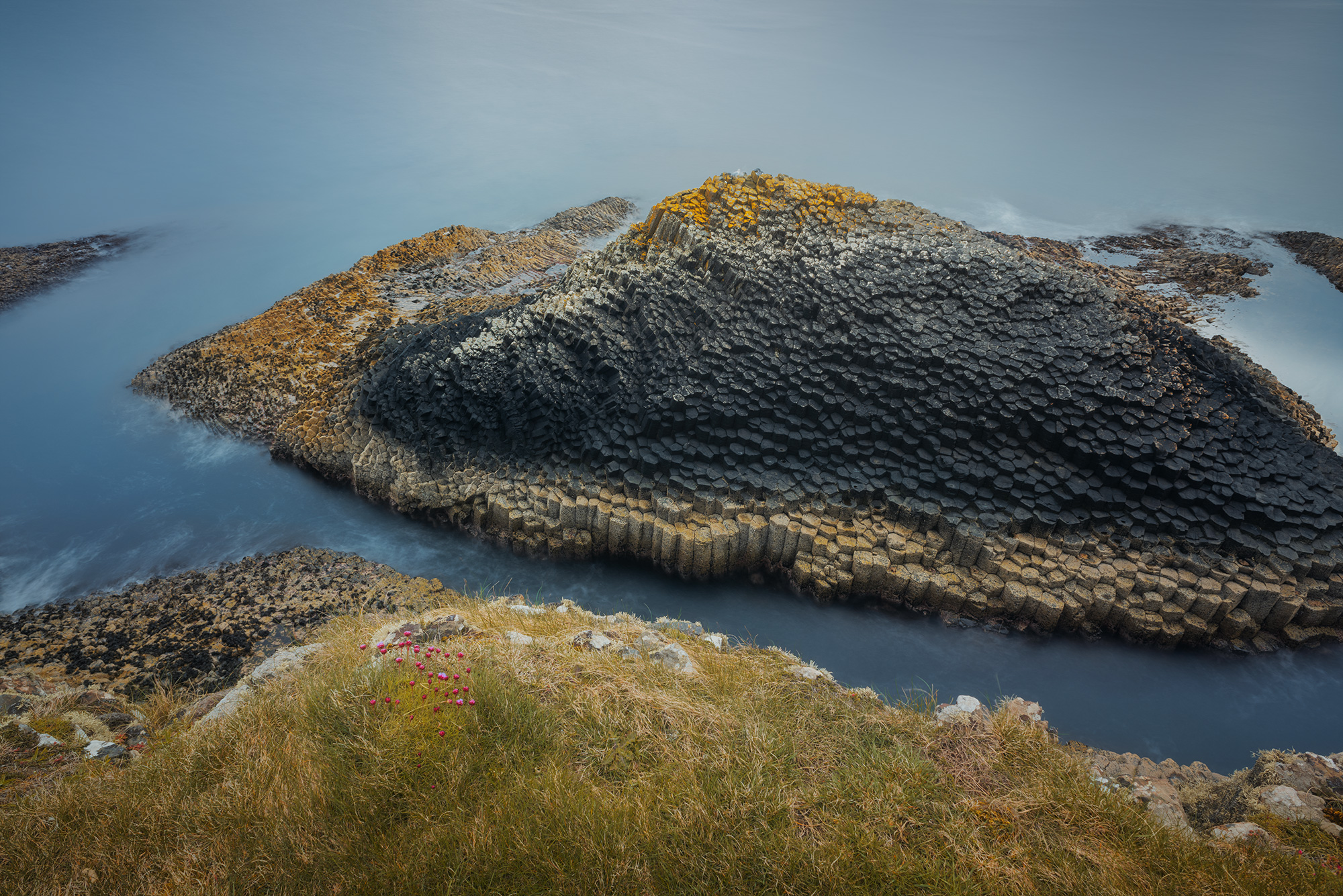 Immerse yourself in the mesmerizing beauty of Staffa Island, an enchanting isle off the coast of Mull Island in Scotland, with this captivating long exposure landscape photography captured by Swiss photographer Jennifer Esseiva and her Nikon D810. Witness the dramatic basaltic formations sculpted by the forces of nature over millennia, standing stoically against the elements. With its long exposure technique, this photograph reveals the dynamic movement of the surrounding waves, adding a sense of motion and drama to the scene. Join Jennifer Esseiva on this visual odyssey as she captures the timeless allure of Staffa Island, where every detail speaks to the power and majesty of the natural world.