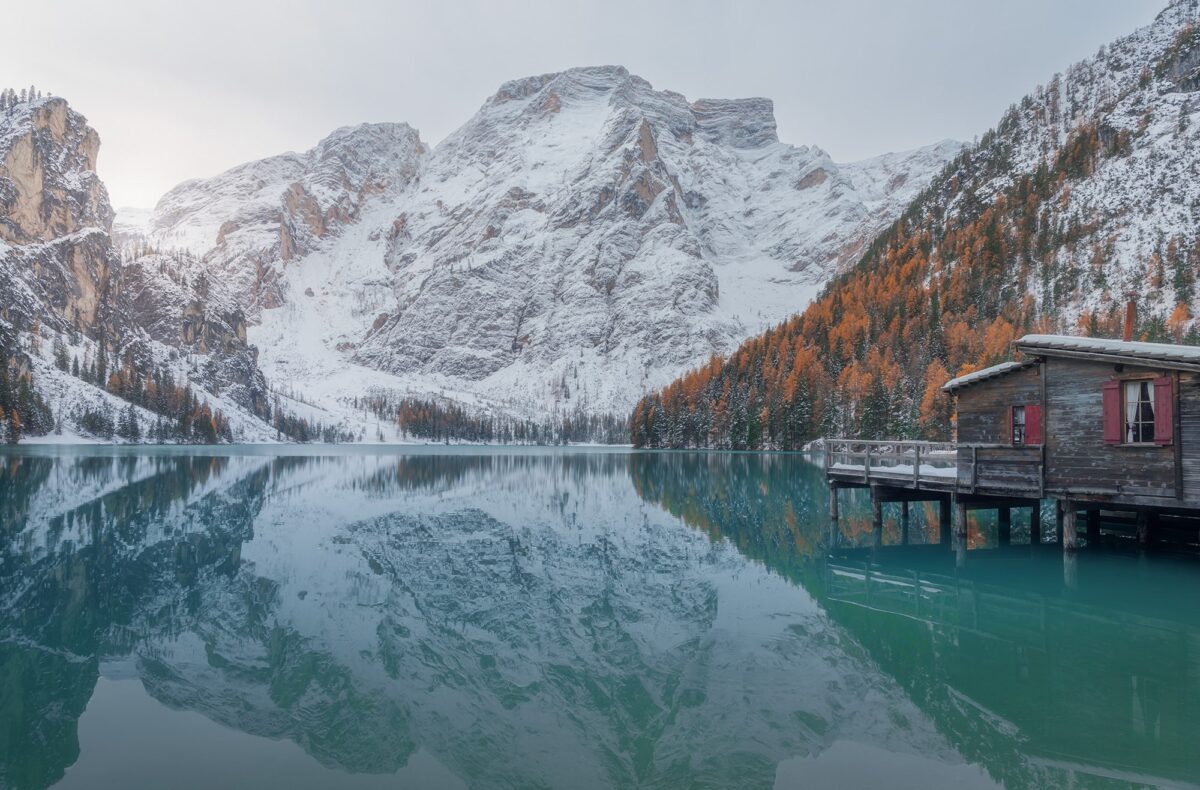 Step into the breathtaking beauty of the Dolomites with this captivating landscape photograph captured by renowned photographer Jennifer Esseiva using her Nikon D810. As the morning light bathes the turquoise waters of Lago di Braies, the surrounding snowy mountains rise majestically, creating a scene of unparalleled natural wonder. Despite the freezing cold of the morning, the serene beauty of the landscape is illuminated by the soft glow of sunrise, casting a warm and inviting ambiance over the scene. Jennifer Esseiva's expert composition and mastery of light capture the essence of this serene moment, inviting viewers to immerse themselves in the tranquil beauty of a sunrise in the Dolomites.