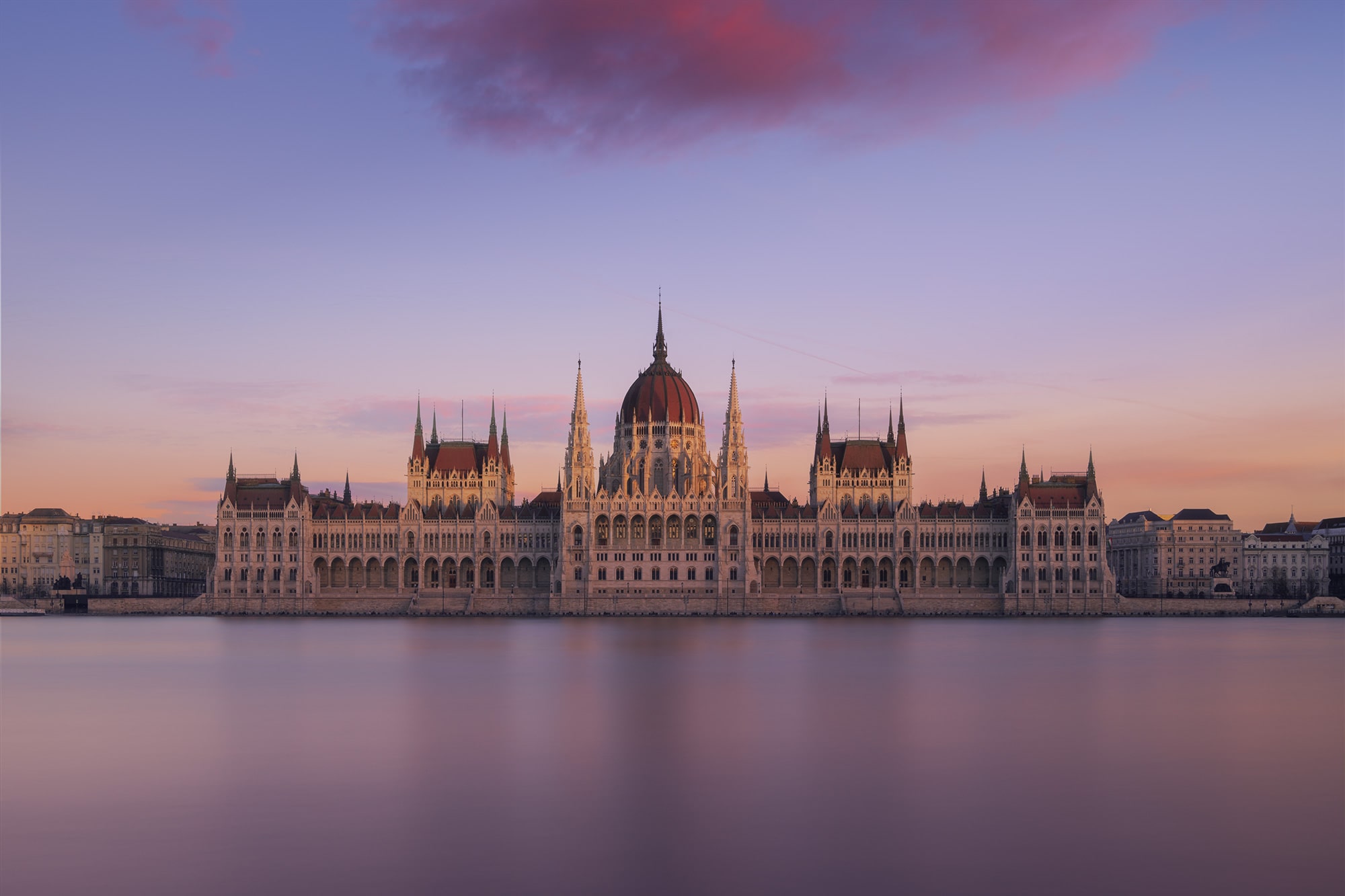 Delight in the mesmerizing beauty of Budapest's Parliament building captured at sunset in this stunning long exposure photograph by travel photographer Jennifer Esseiva using her Nikon Z8. The warm hues of the setting sun cast a golden glow over the majestic architecture, while the gentle movement of the clouds adds a sense of serenity to the scene. From the intricate details of the building's façade to the tranquil waters of the Danube River below, every element is expertly composed to evoke a feeling of awe and wonder. Immerse yourself in the breathtaking panorama of Budapest's skyline as captured by Jennifer Esseiva, and experience the magic of sunset over the Parliament.
