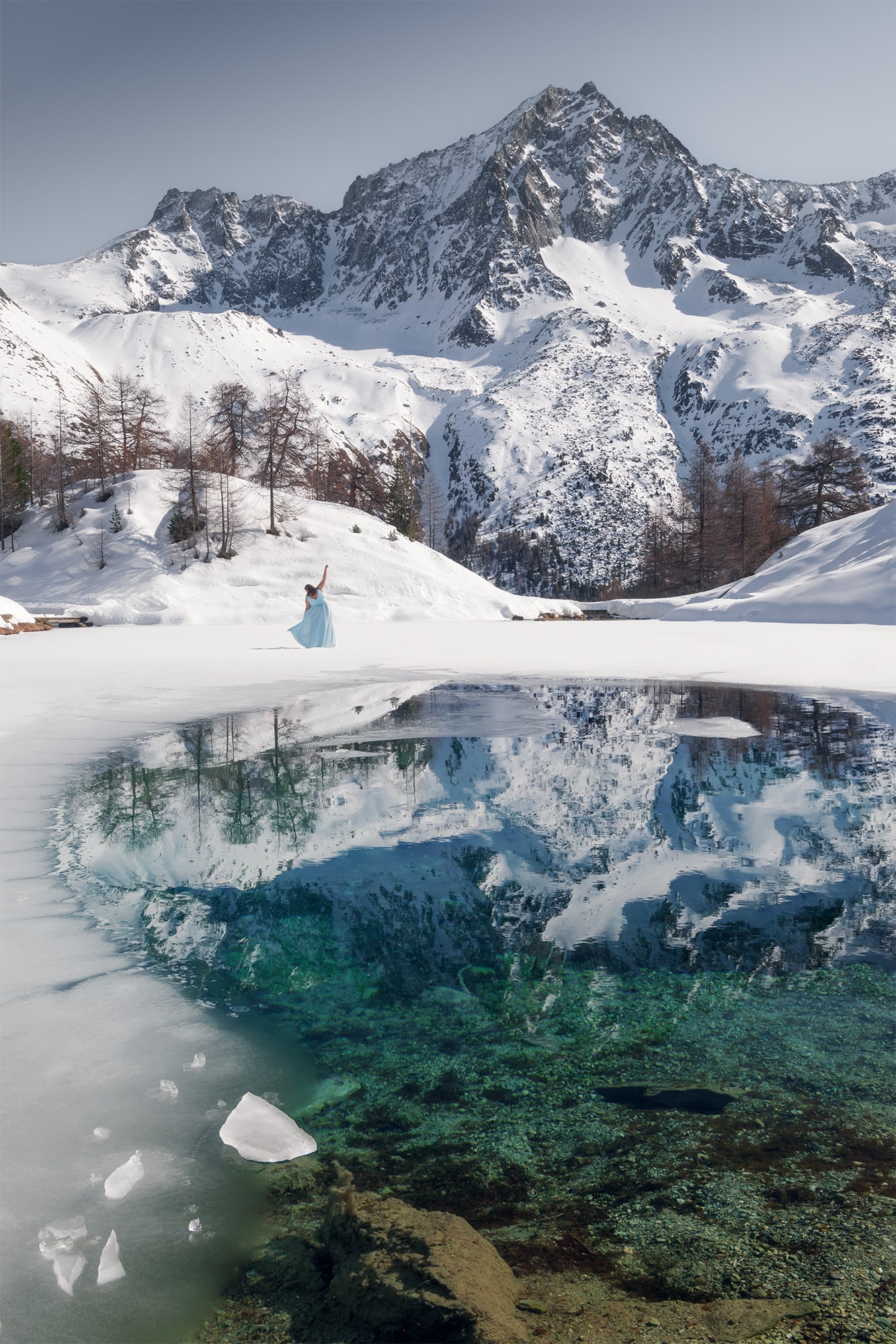 Immerse yourself in the enchanting world of Swiss landscape photography with this captivating self-portrait by Jennifer Esseiva. The renowned Swiss photographer gracefully dances atop the frozen Lac Bleu in Arolla, amidst the majestic Swiss Alps. Jennifer, adorned in a fairytale turquoise dress, adds a touch of magic to the pristine snow-covered landscape. Taken with her trusted Nikon Z8 camera, this stunning photograph captures the ethereal beauty of the Swiss Alps, inviting viewers to experience the wonder of nature through Jennifer's lens.