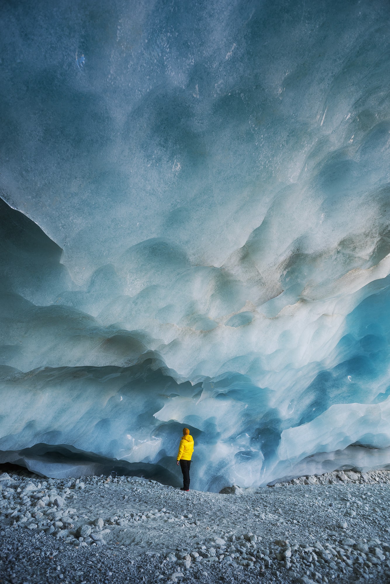 Immerse yourself in the grandeur of the Zinal Glacier Ice Cave, as showcased in this epic landscape photograph. Against the backdrop of the towering ice wall, a mountaineer clad in a vibrant yellow jacket adds scale and intrigue to the scene. Located in the breathtaking Swiss Alps, this dramatic view captures the essence of nature's majesty. Expertly captured by photographer Jennifer Esseiva using her Nikon D810, this image invites you to explore the wonders of the Swiss wilderness.