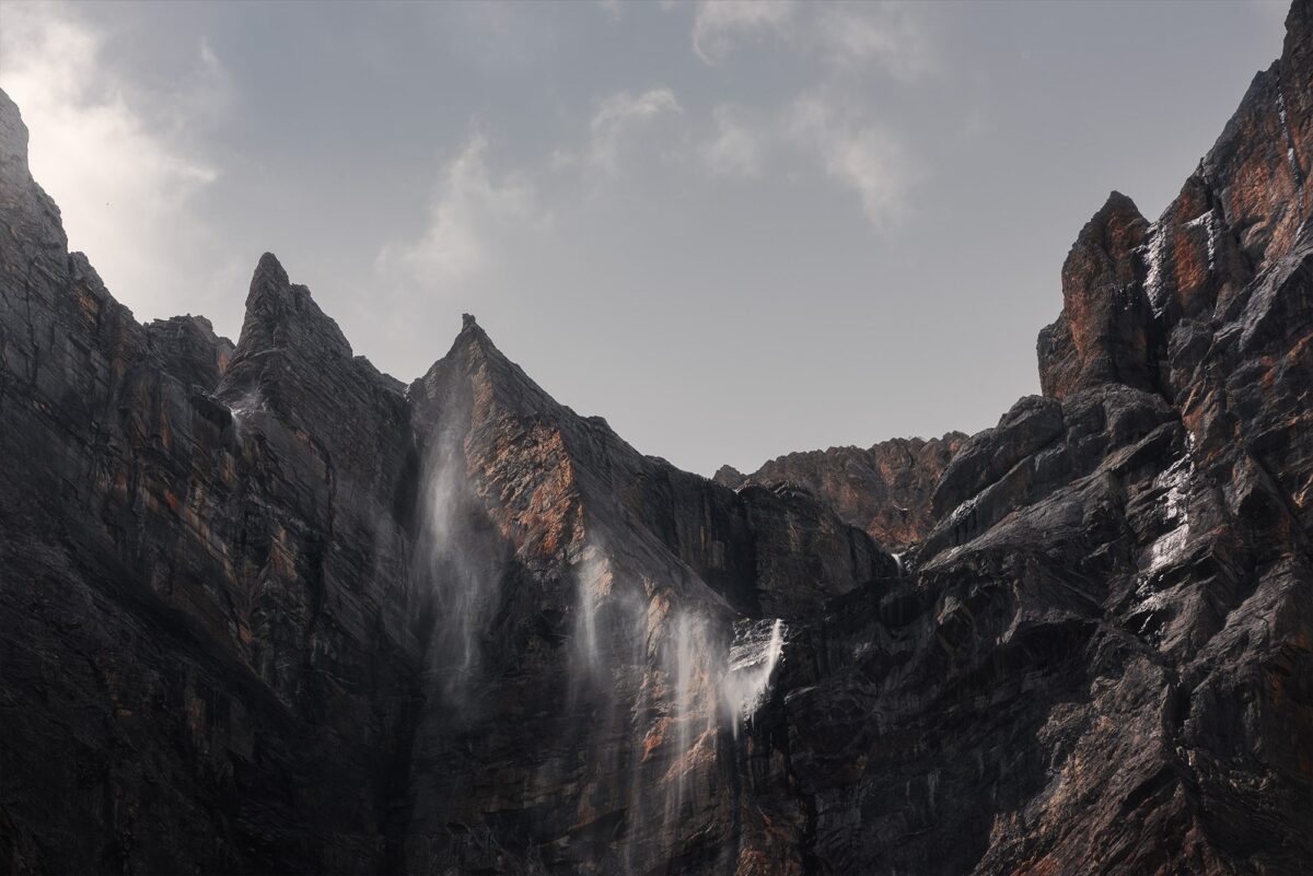 Marvel at the breathtaking landscape captured in this dramatic photography featuring a rock wall and wind-blown waterfall in the Swiss Alps. With sheer magnificence, nature's forces collide in this epic scene, expertly captured by photographer Jennifer Esseiva using her Nikon D810. Prepare to be mesmerized by the raw power and stunning beauty of Switzerland's alpine wonders.