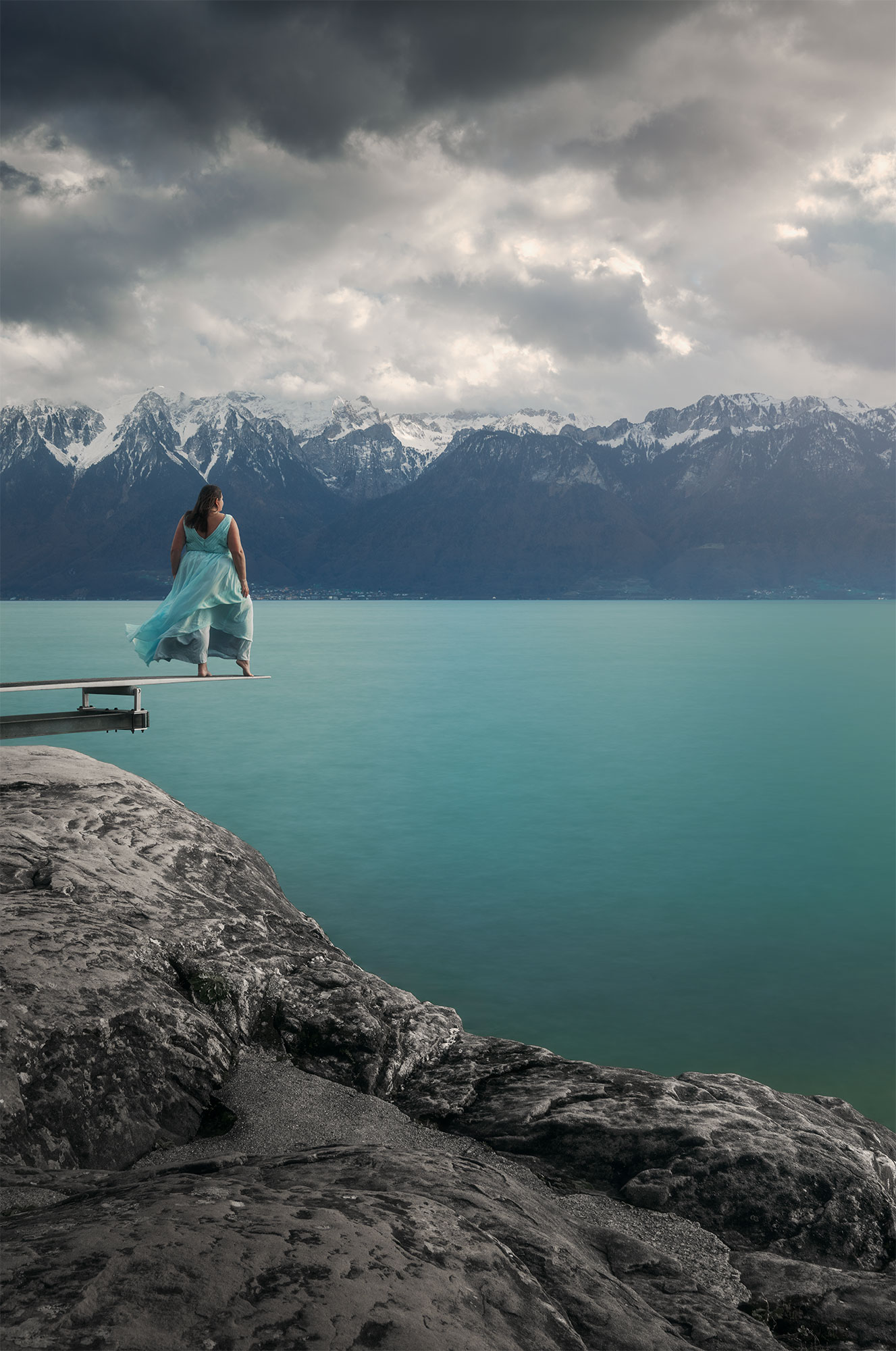 Step into the enchanting world of Swiss landscape photographer Jennifer Esseiva through this captivating self-portrait. Adorned in a stunning turquoise ice blue dress reminiscent of a Disney princess, she stands poised on a diving board in Saint-Saphorin, amidst the breathtaking Lavaux vineyards of Switzerland. With Geneva Lake as her backdrop, Jennifer invites you to join her in this mesmerizing moment, where nature's beauty and artistic expression converge seamlessly. Explore the wonder of Switzerland's landscapes through the lens of this talented photographer.