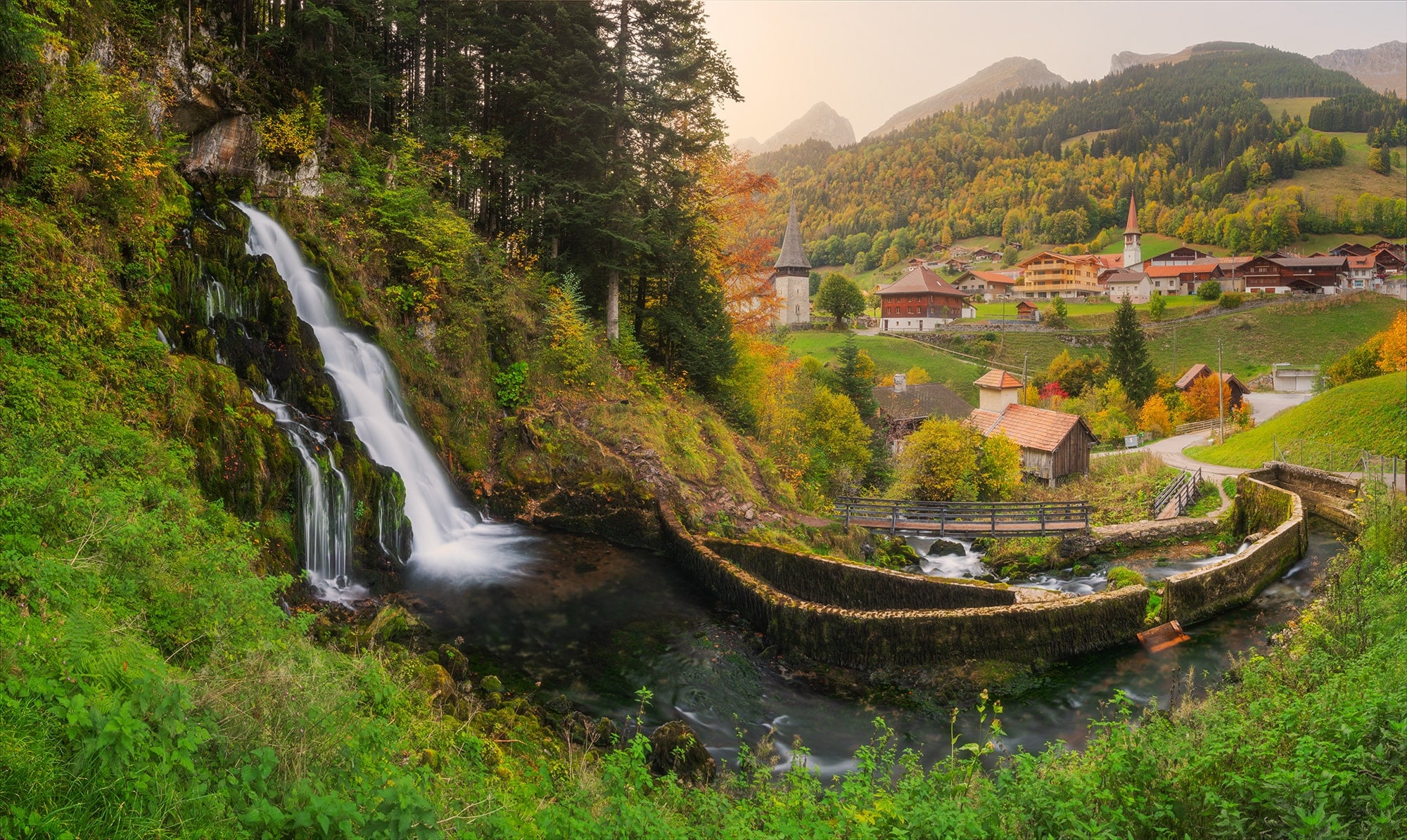 Experience the breathtaking beauty of Jaun village and its surrounding landscape in autumn, captured in this stunning panorama and long exposure photograph. Located in Canton Fribourg, Switzerland, this mesmerizing image showcases the picturesque waterfall alongside the charming village of Jaun. Immerse yourself in the serene atmosphere and vibrant hues of autumn foliage, beautifully frozen in time through long exposure photography. Explore the natural splendor of Switzerland's landscapes in this captivating panorama by