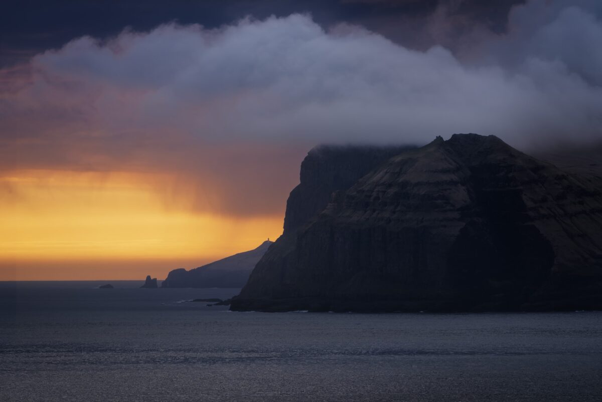 Sunset behind Mykines Island, Faroe Islands, with warm light over rugged coastal landscape.