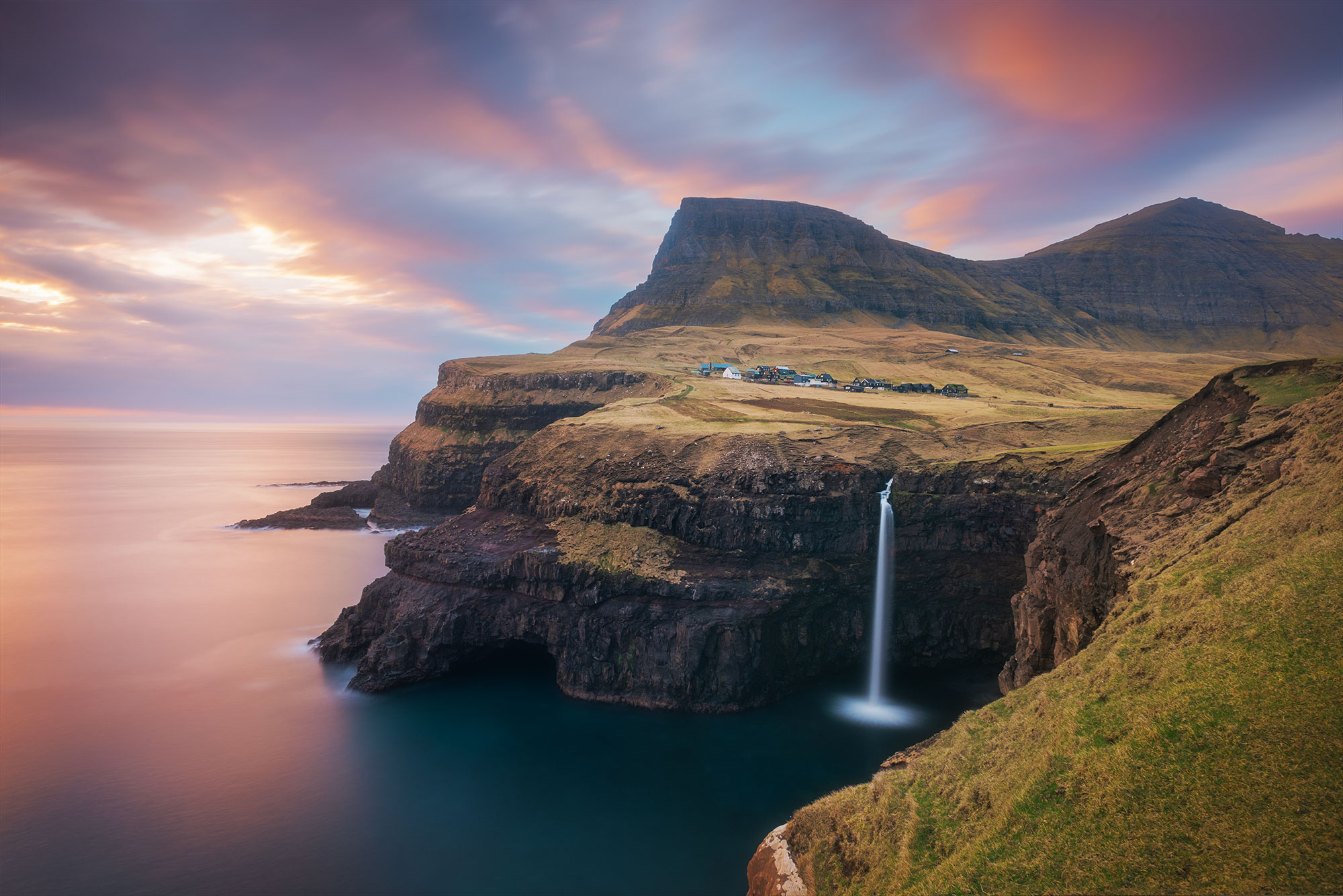 Indulge in the captivating artistry of landscape photography with this mesmerizing image capturing the sunset over the picturesque village of Gásadalur and the iconic Múlafossur waterfall in the Faroe Islands. Immortalized by landscape photographer Jennifer Esseiva, this stunning composition encapsulates the serene beauty of nature's spectacle. Let yourself be transported to this remote paradise as you admire the interplay of light and shadow against the rugged cliffs and cascading waters.