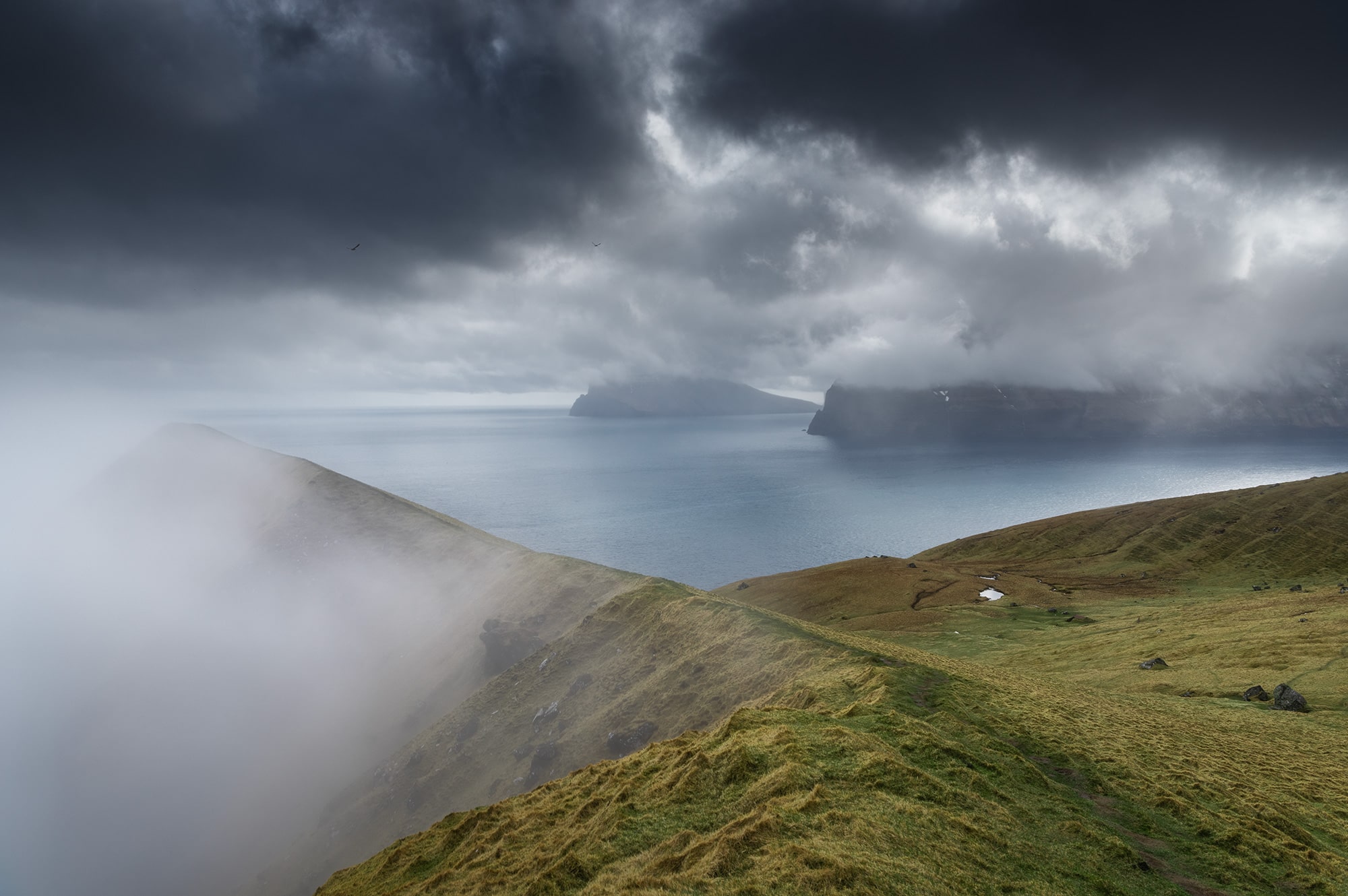 Embark on a visual odyssey through the captivating landscapes of the Faroe Islands with this striking landscape photograph. Behold the dramatic vista of the island of Kalsoy under a dark and brooding sky, characteristic of the epic scenery of this remote archipelago. This mesmerizing image encapsulates the raw beauty and rugged charm of the Faroe Islands, inviting viewers to immerse themselves in its breathtaking allure. Experience the magic of nature's drama unfolding through the lens of this evocative landscape photograph. Explore the timeless allure of the Faroe Islands in this captivating portrayal of its epic landscapes.