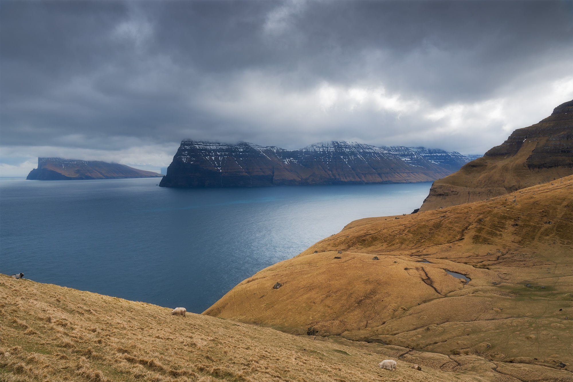 Embark on a visual journey through the captivating landscapes of the Faroe Islands with this stunning landscape photograph. Witness the dramatic vista of Kalsoy Island under a dark and brooding sky, characteristic of the epic scenery of this remote archipelago. This mesmerizing image captures the raw beauty and rugged charm of the Faroe Islands, inviting viewers to immerse themselves in its breathtaking allure. Experience the magic of nature's drama unfolding through the lens of this evocative landscape photograph. Explore the timeless allure of the Faroe Islands in this captivating portrayal of its epic landscapes.