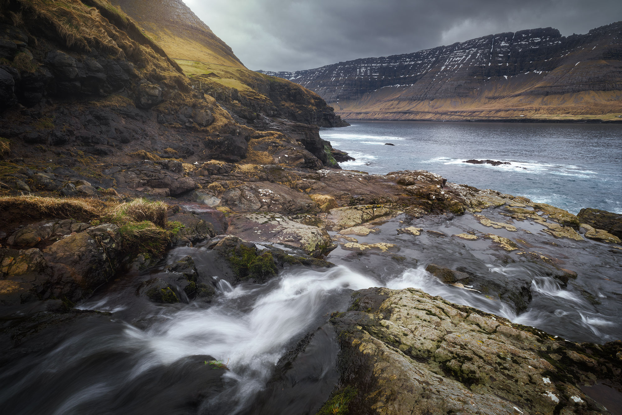 Experience the captivating beauty of Viðoy Island in the Faroe Islands through the lens of long exposure landscape photography. This stunning image captures the serene flow of a river as it meanders from the picturesque village of Viðareiði to the expansive ocean. Immerse yourself in the tranquil atmosphere of this remote island destination, where rugged cliffs meet the soothing waters below. Explore the dynamic movement captured in this long exposure photograph, offering a glimpse into the timeless charm of Viðoy Island's natural landscapes.