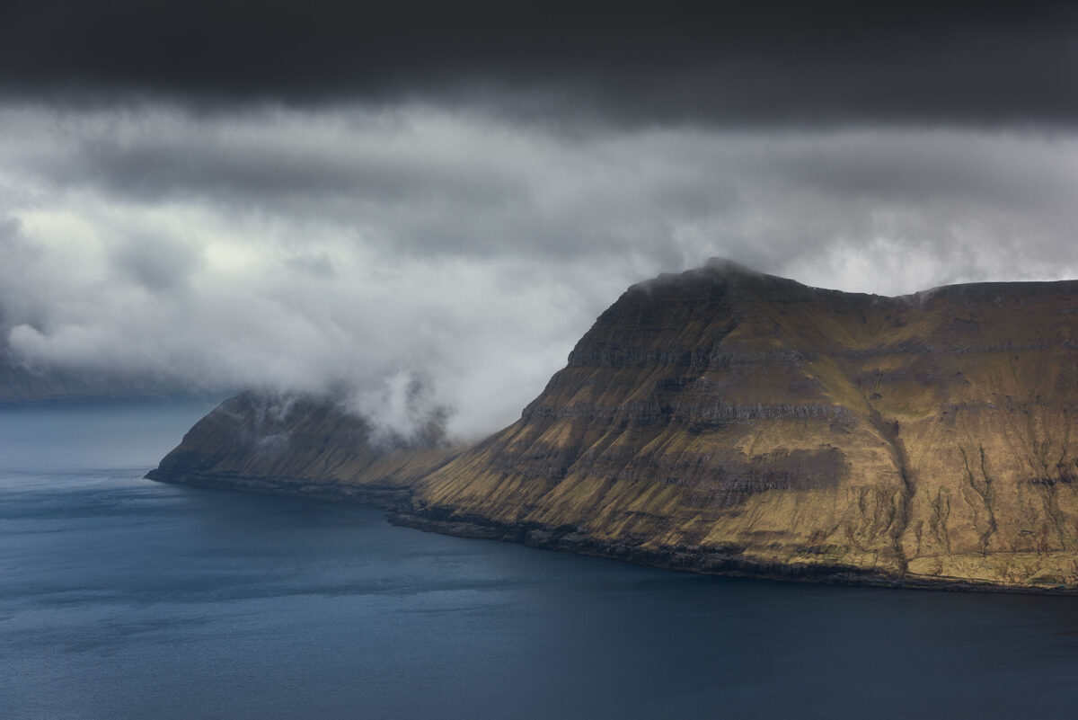 Dramatic cloudy landscape in the Faroe Islands, with rugged terrain and moody atmosphere.
