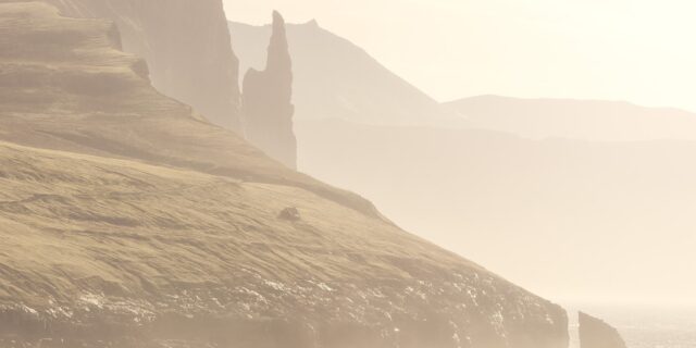 Trøllkonufingur sea stack at sunrise in the Faroe Islands, with warm light on rugged cliffs and ocean.