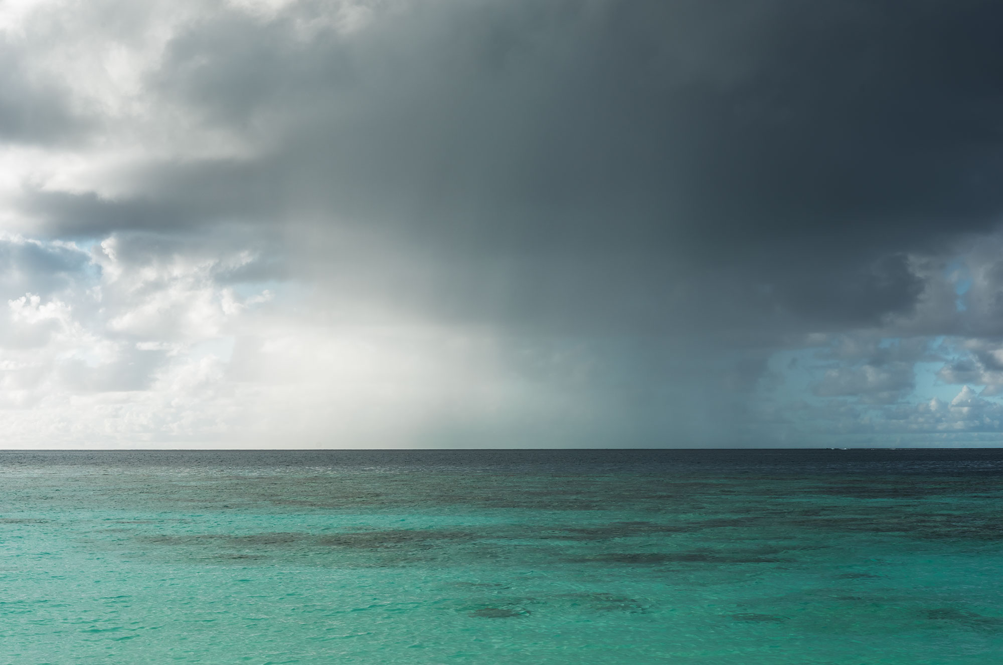 Landscape photograph capturing the stunning turquoise sea of the Maldives during a rainstorm, creating a dramatic and serene scene.
