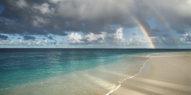 Landscape photograph showcasing the paradise beach of Thudufushi resort in the Maldives, featuring a stunning double rainbow in the sky.