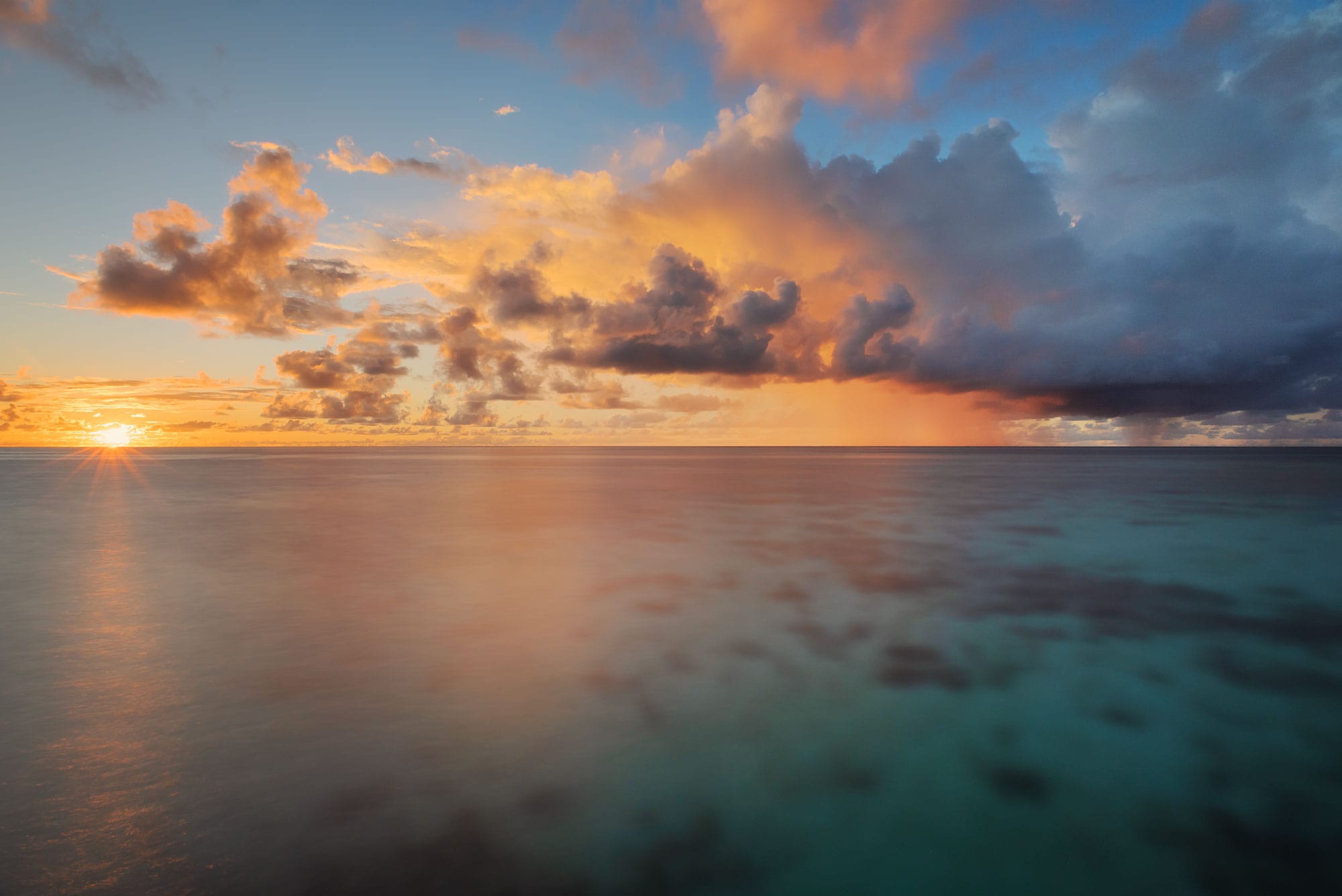 Landscape photograph capturing a romantic and paradisiac sunset in the Maldives, taken on the island of Thudufushi, showcasing vibrant hues painting the sky and reflecting off the tranquil waters.