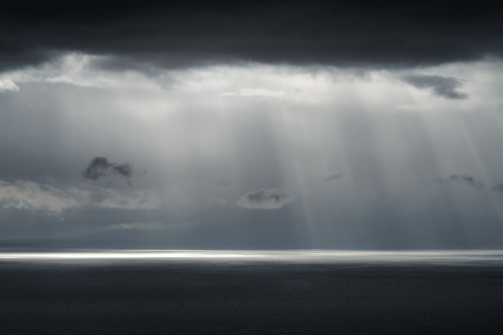 Scenic landscape photograph capturing dramatic light above Lake Geneva on a rainy day. A ray of light pierces through the clouds, illuminating the water. Taken in Chexbres, Lavaux, Switzerland, by Swiss photographer Jennifer Esseiva using her Nikon Z8.