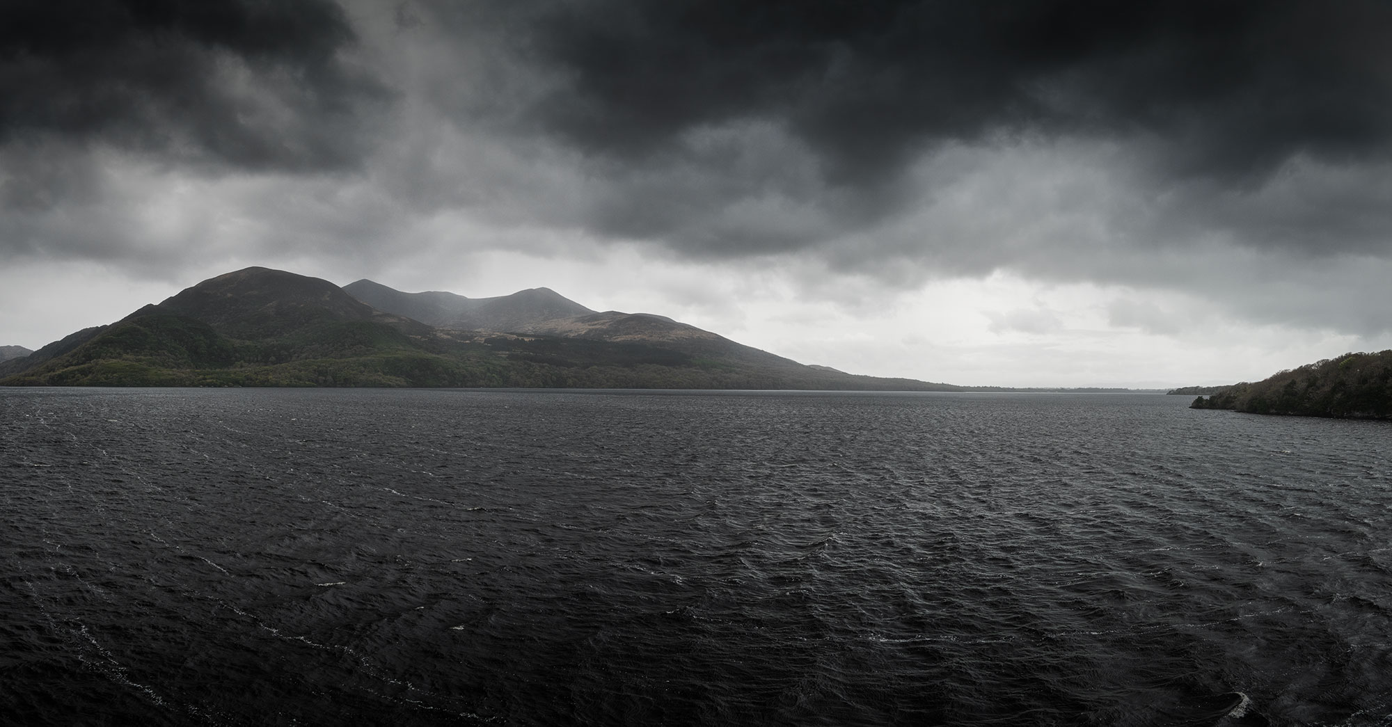 A panoramic landscape photograph of the Lakes of Killarney in Ireland, showcasing a dramatic sky on a rainy day. The image captures the wild beauty of the Wild Atlantic Way, taken with a Nikon Z8 camera.