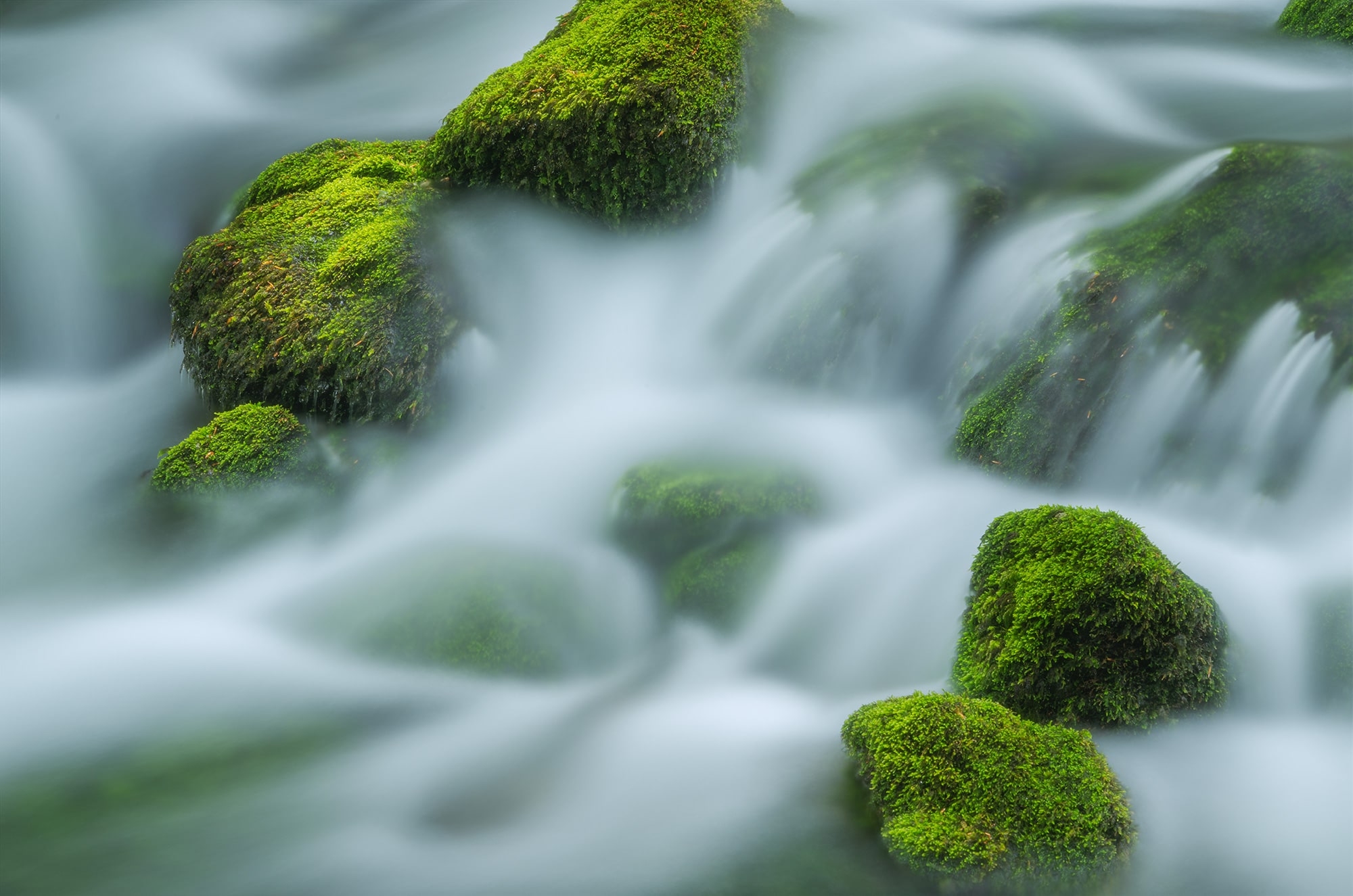 Captivating long exposure river photography of moss-covered rocks in Vallorbe, Switzerland. The ethereal ambiance gives the scene a fairytale-like appearance. Taken with a Nikon Z8, this image captures the tranquil beauty of nature in motion.