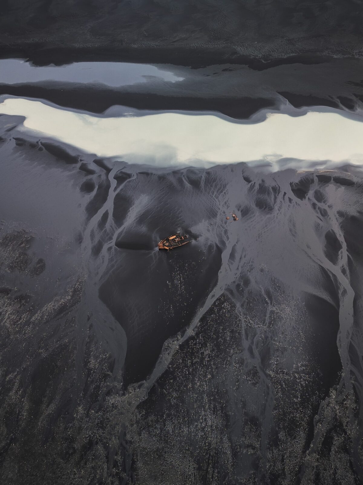 Drone photography in Iceland showing a dramatic shipwreck on a black sand beach in South Iceland, captured by Jennifer Esseiva to highlight the raw beauty of Iceland’s coastline.
