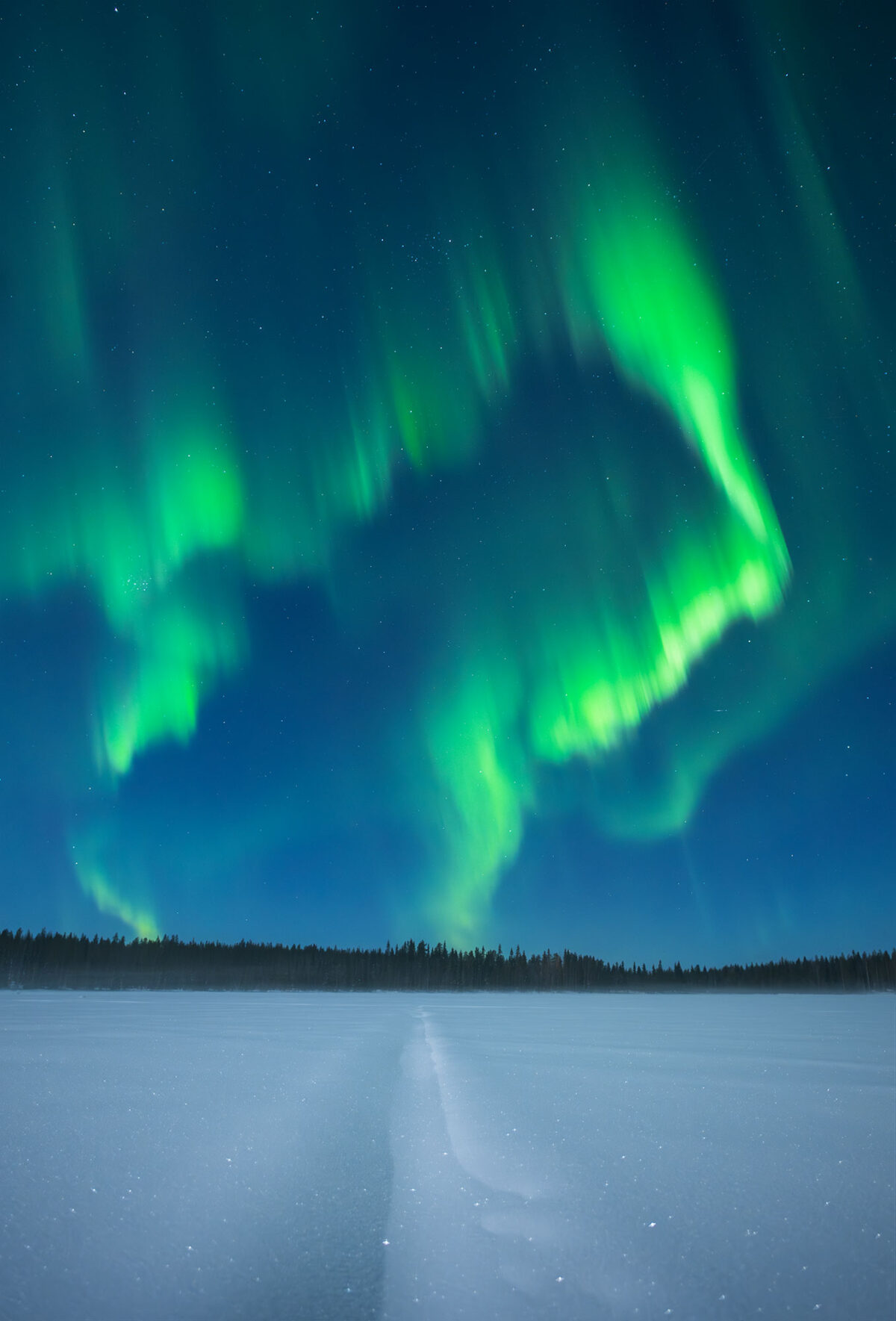 A mesmerizing display of the Northern Lights over a frozen lake in Levi, Lapland, Finland. This breathtaking night photography scene captures the aurora borealis dancing above the snow-covered forest, reflecting on the icy surface of the lake. The untouched winter landscape, combined with the magic of long-exposure photography, showcases the beauty of Lapland’s Arctic wilderness. Levi is one of Finland’s best destinations for Northern Lights photography, offering pristine nature and dark skies for an unforgettable aurora experience.