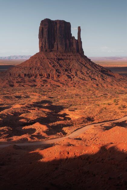 Vertical photography of Monument Valley at sunset in Arizona, USA, showcasing the towering sandstone formations against a fiery sky. The striking silhouette of the mesas and spires stands in contrast to the rich, warm colors of the setting sun, creating a stunning image that captures the essence of the American Southwest. The vibrant hues of orange, red, and purple reflect the tranquil yet powerful beauty of this iconic desert landscape.