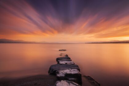 Landscape photography of Lake Geneva from Préverenges Beach at sunset, with long exposure and the Swiss Alps in the background.