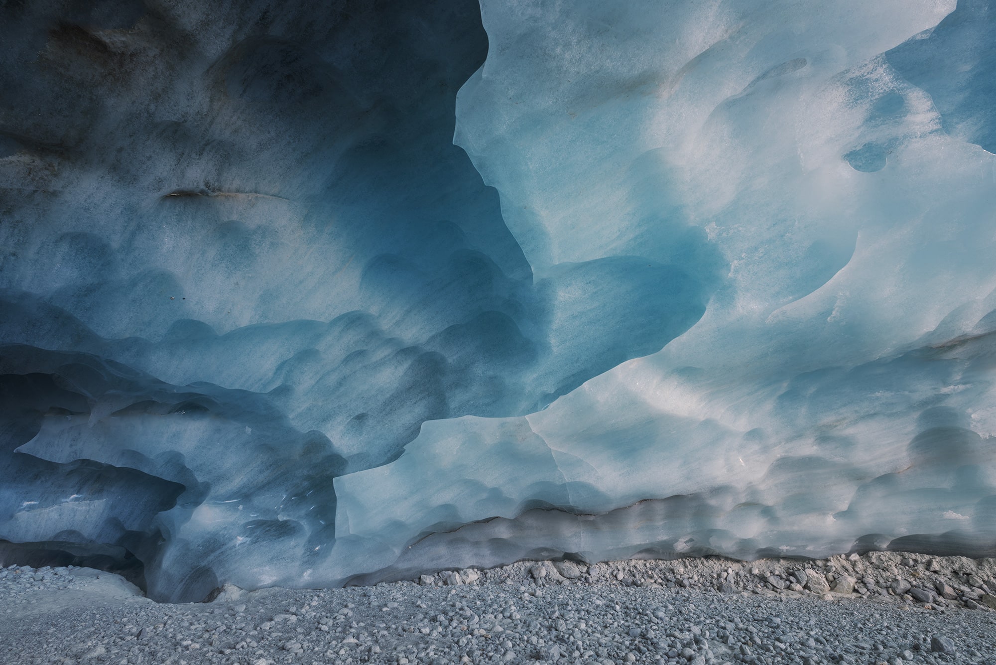 Wall of ice inside the Zinal glacier cave, Valais, Switzerland, captured in 2022. The ice rises from the ground in a striking organic shape, as if growing from the earth itself. Its smooth, translucent textures and bluish tones highlight the sculptural power of nature inside this Swiss alpine cave.