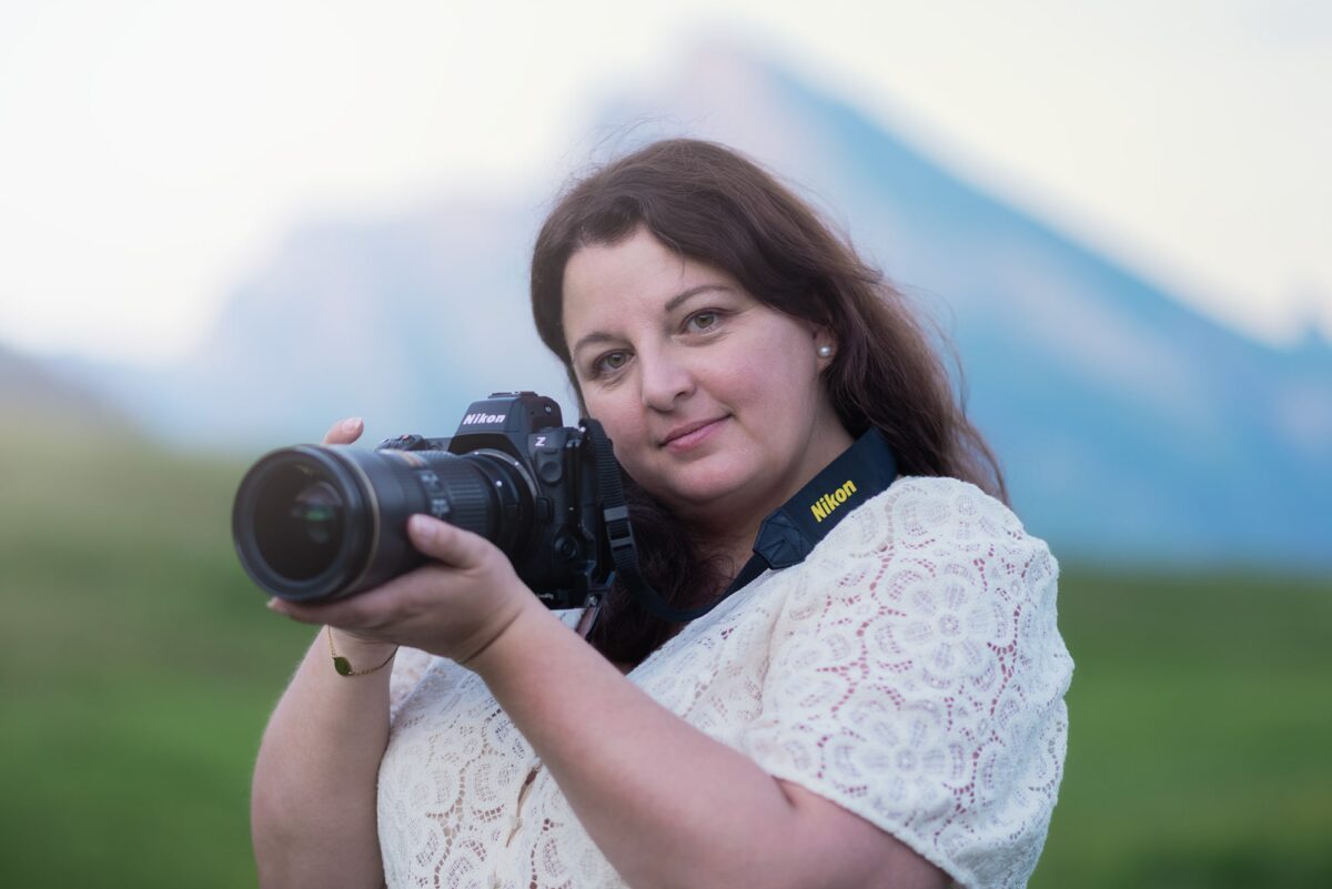 Portrait photo of Swiss landscape photographer Jennifer Esseiva holding her Nikon camera, captured in natural light with a scenic background.
