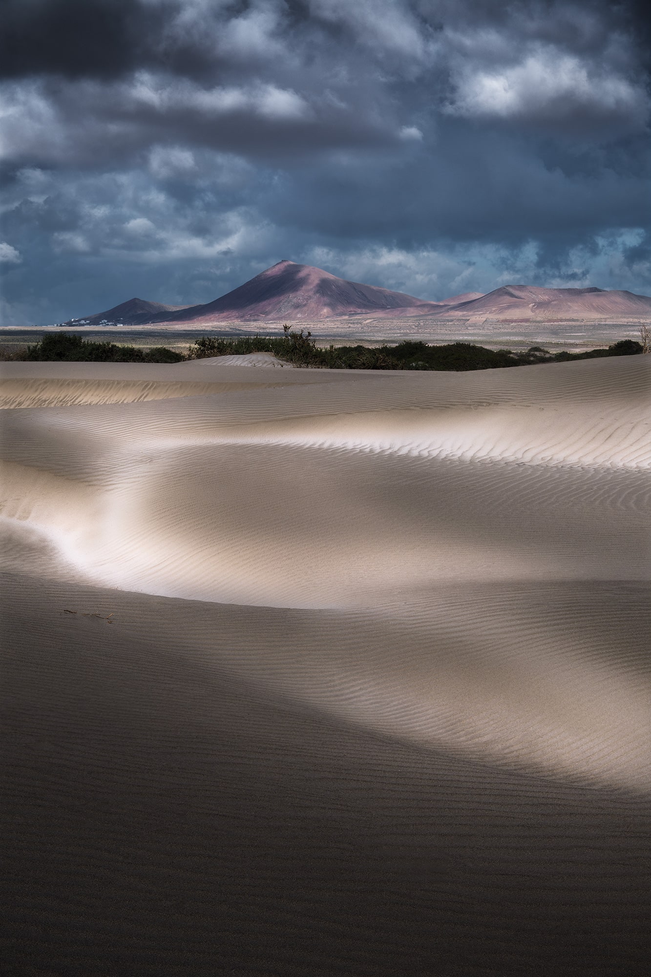 Morning light at the Famara Dunes in Lanzarote, Canary Islands, with artistic sand patterns and a scenic view of volcanoes under a dramatic sky.