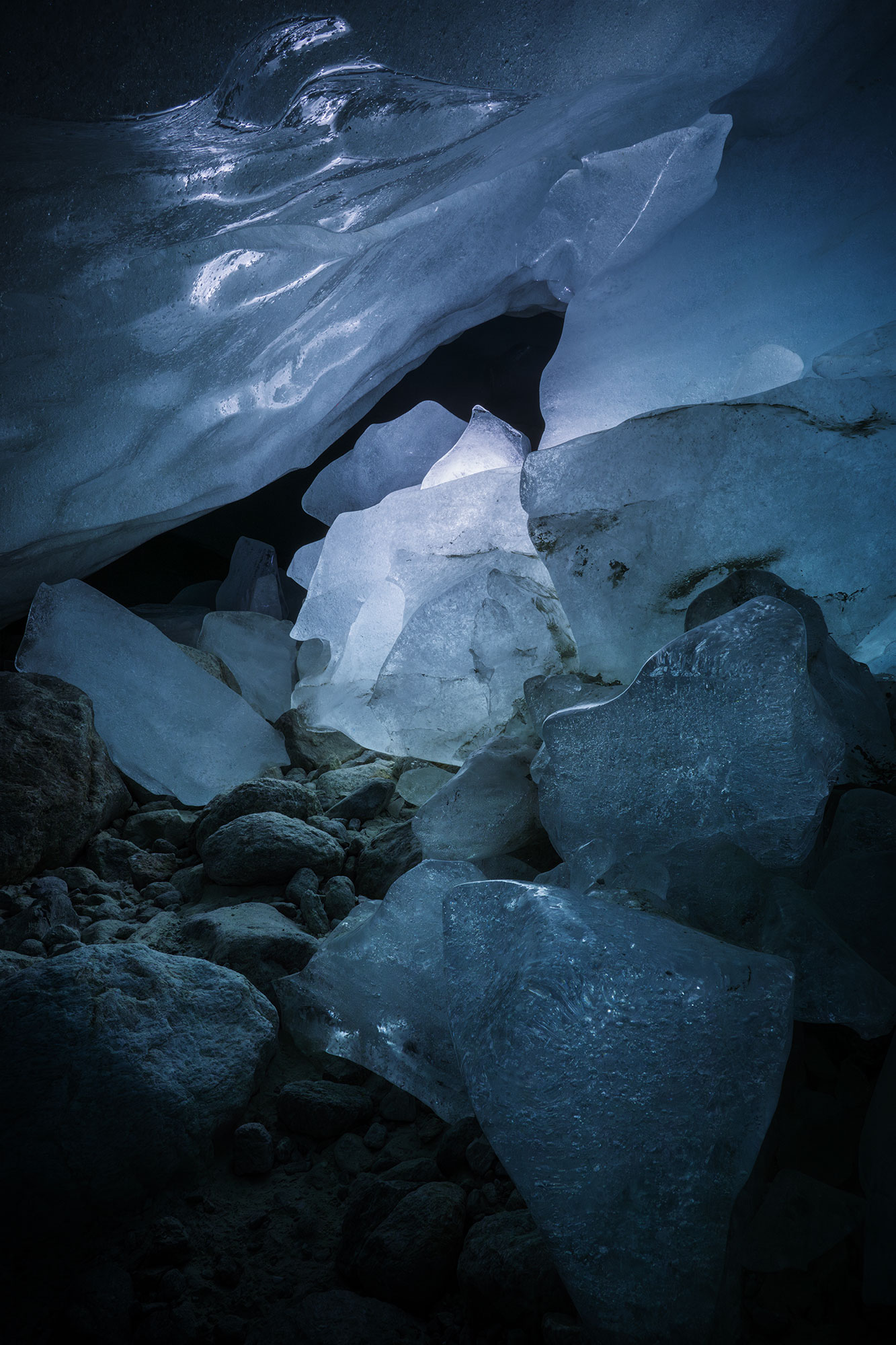 Inside the Zinal glacier ice cave in Valais, Switzerland, a glowing light reveals the intricate textures of a massive ice formation. The frozen walls shimmer in deep blue tones, capturing the timeless beauty of this natural wonder. Nestled in the heart of the Swiss Alps, this ephemeral cave offers a glimpse into the ever-changing world of glaciers.