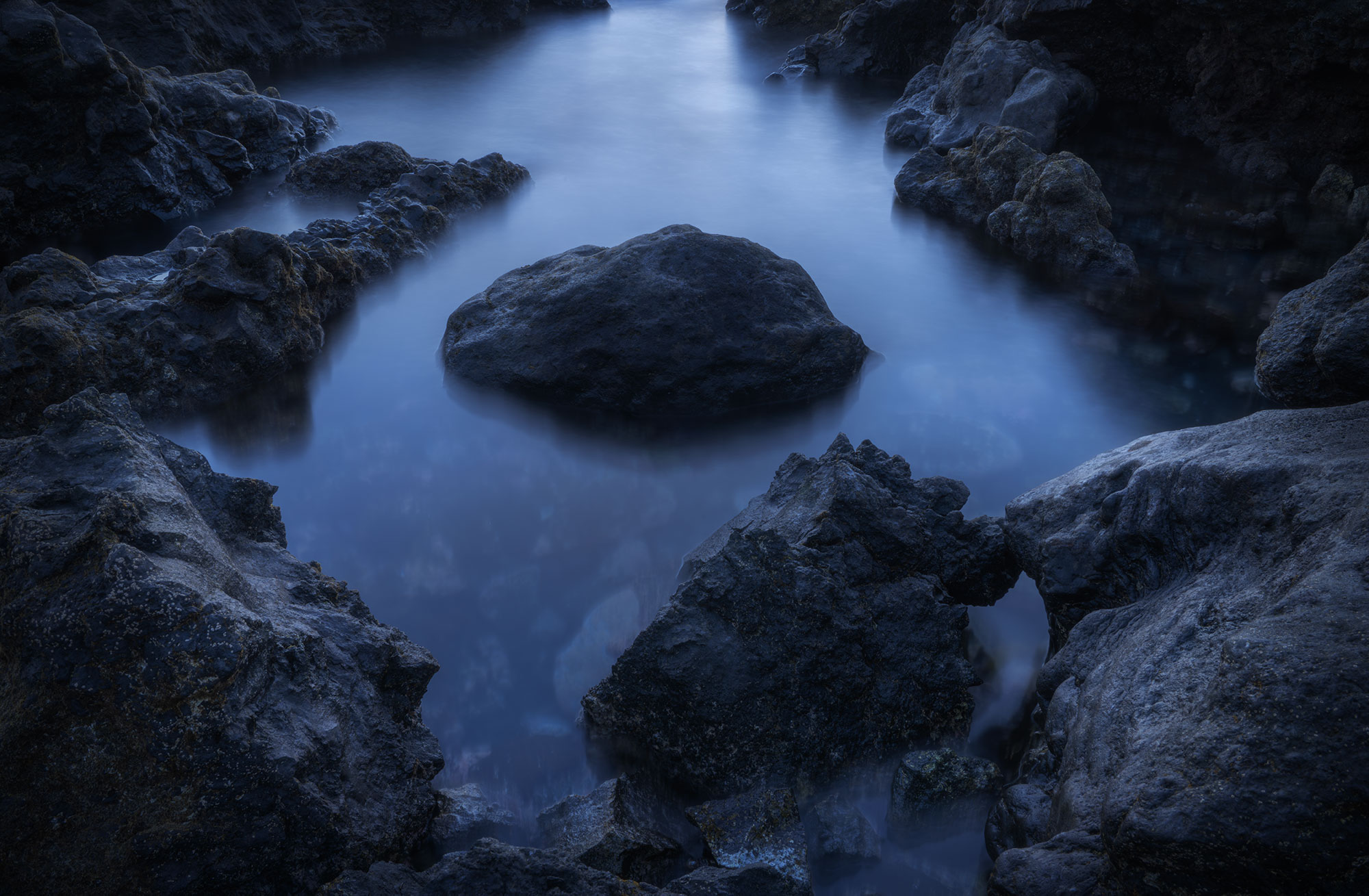 Long exposure seascape at Montaña Bermeja in Lanzarote, Canary Islands, showing black volcanic stones under soft blue hour light for a minimalist nature landscape photograph.