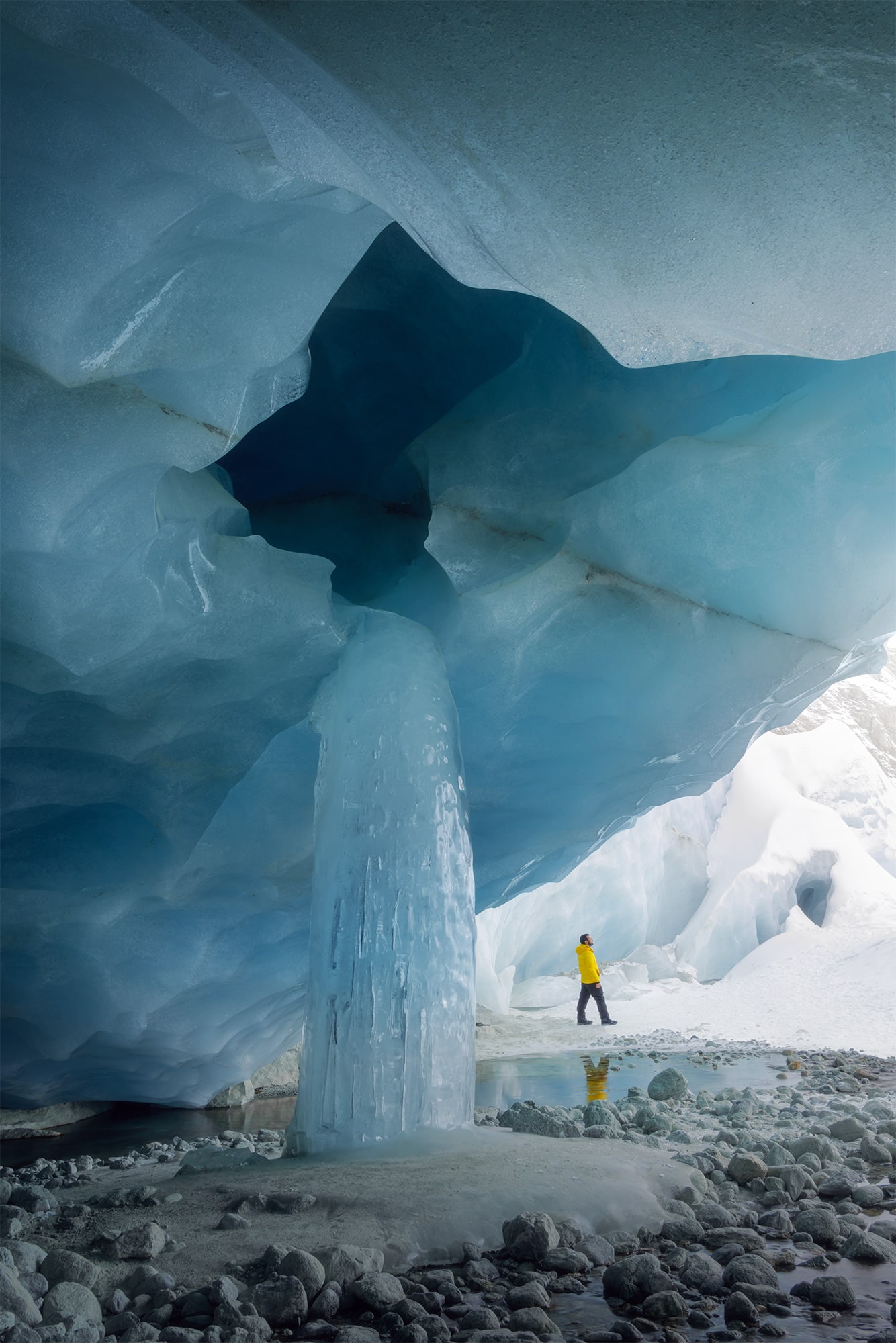 Zinal ice cave in Switzerland, located in the canton of Valais, featuring a frozen waterfall and a landscape photographer wearing a yellow jacket inside the glacier.