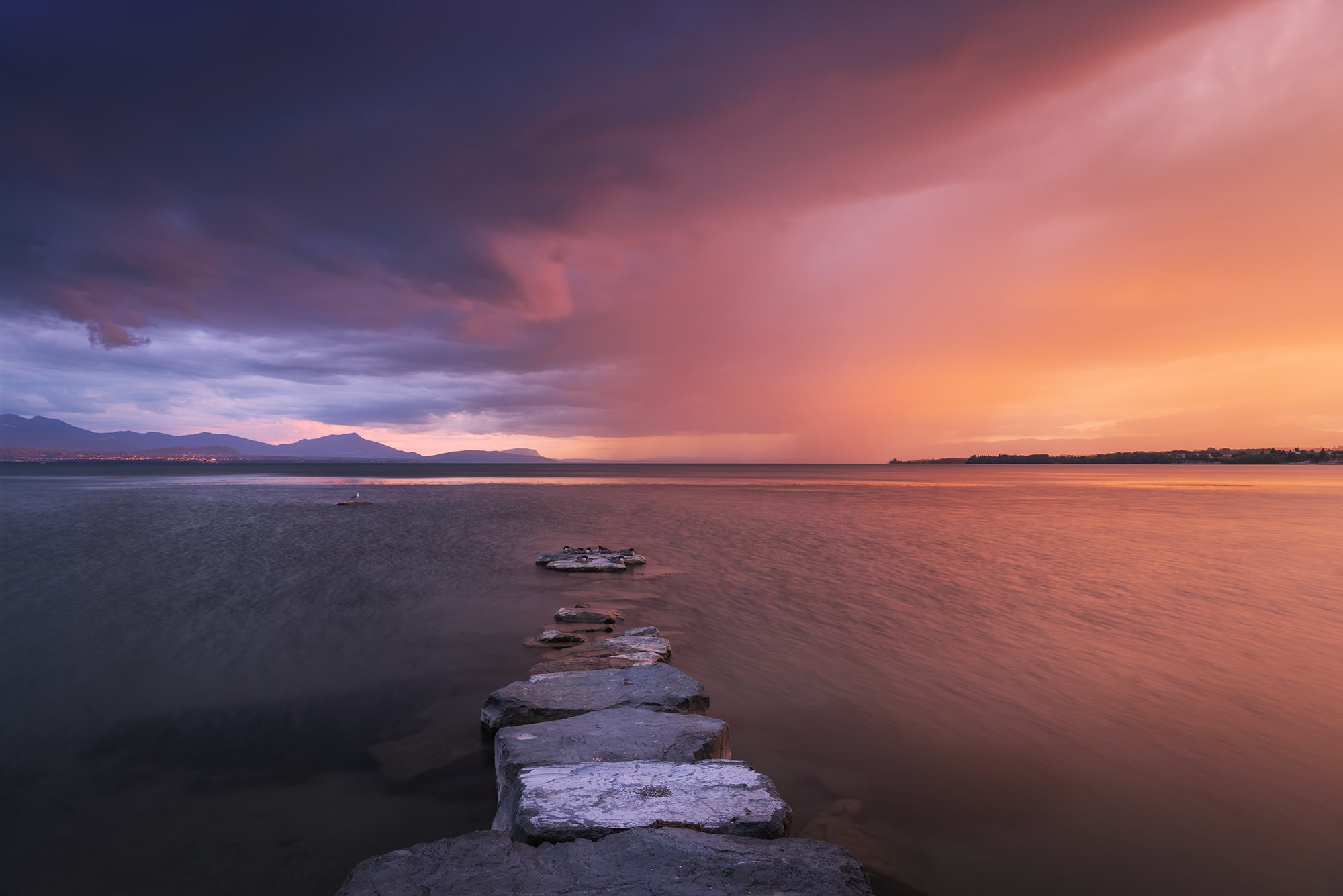 Landscape photography of a sunset over Geneva Lake from Lausanne, Switzerland, with large pink-colored clouds in the sky.