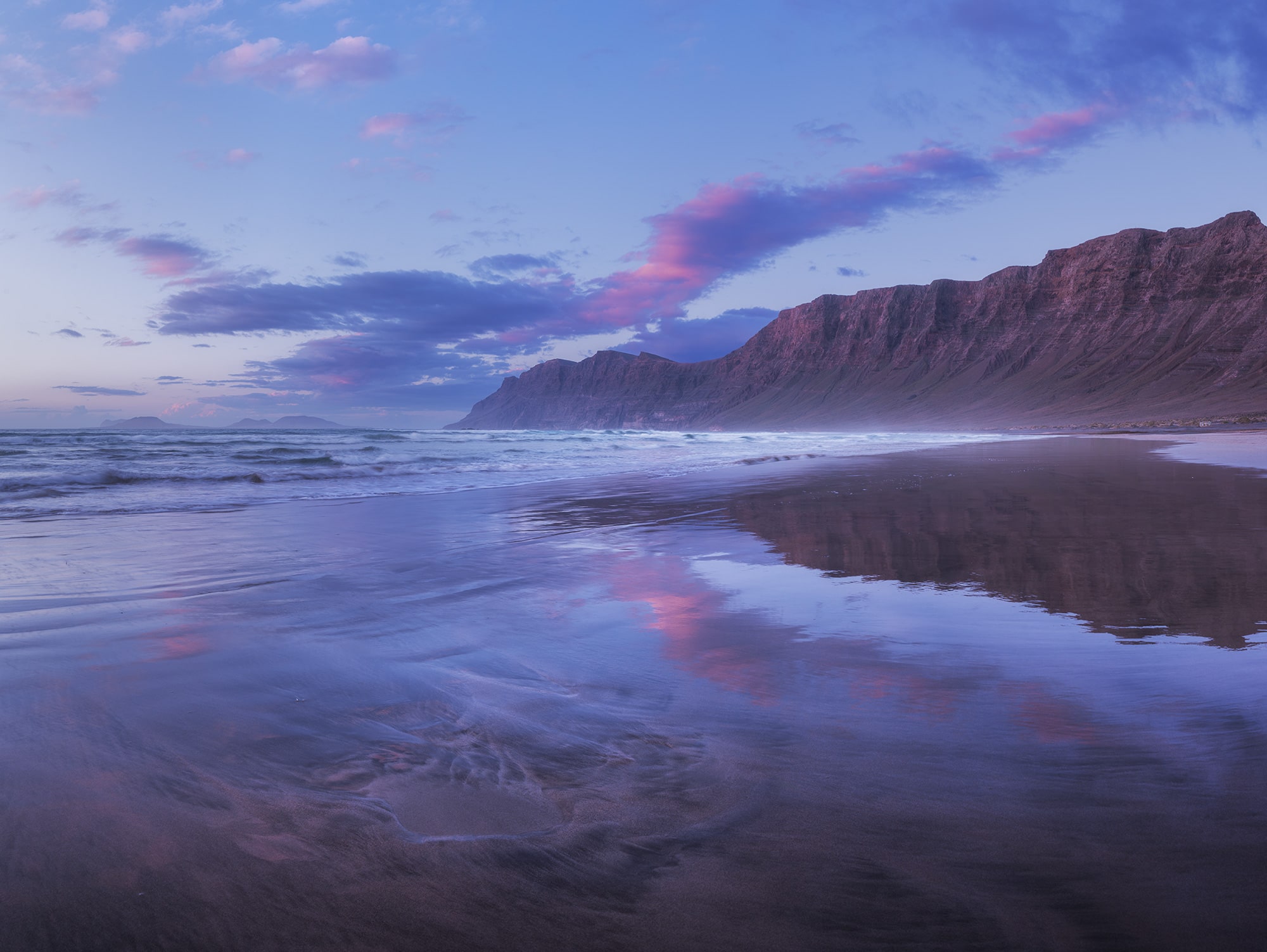 Blue hour at Famara Beach in Lanzarote, Canary Islands, featuring soft light and a perfect reflection on the wet sand with mountains in the background.