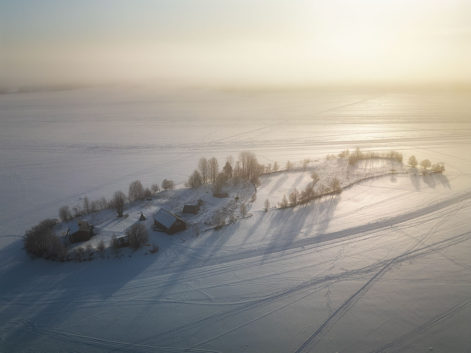 Drone photograph of Kotisaari Island in Rovaniemi just after sunrise, surrounded by a frozen lake and winter fog.