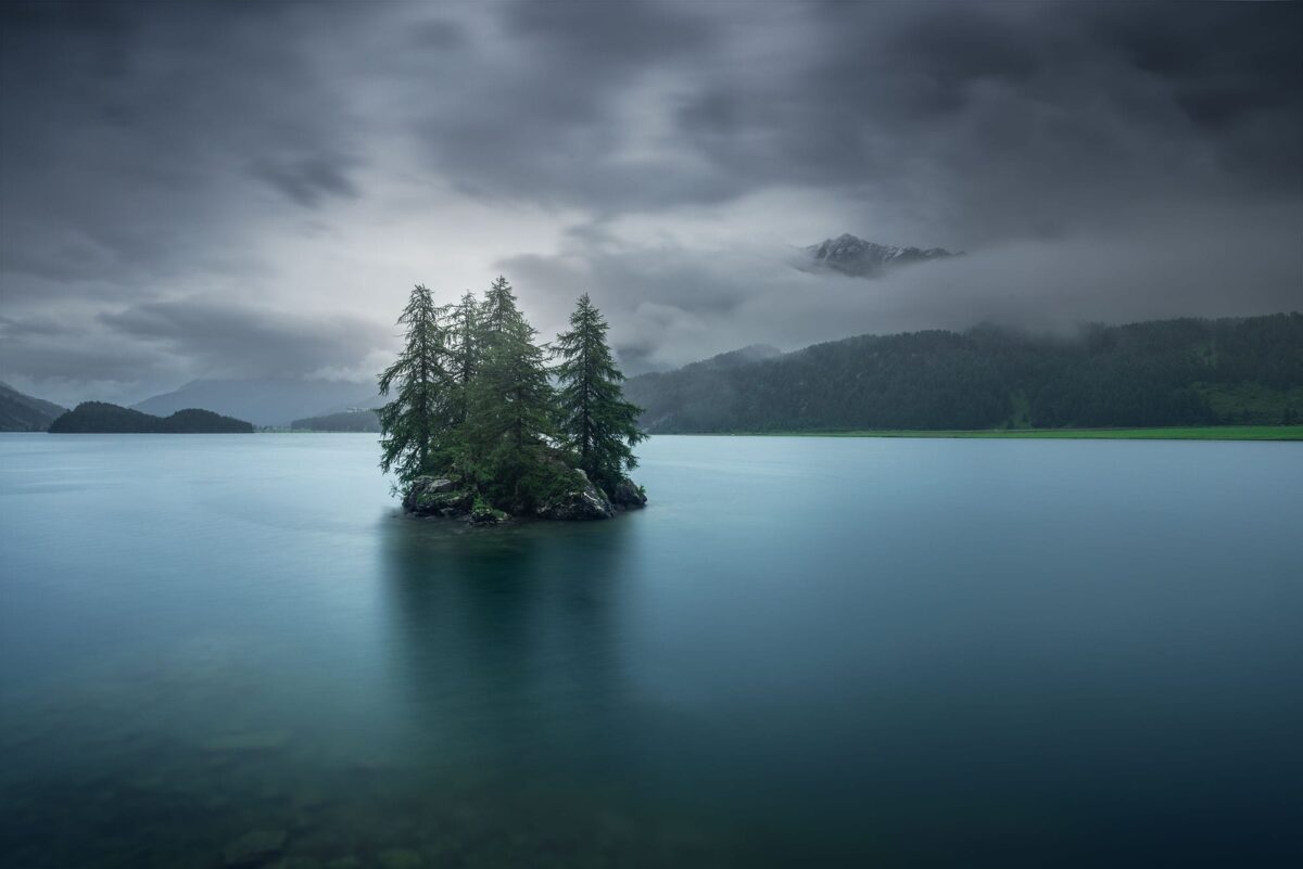 Long exposure landscape photography at Silsersee near St. Moritz, Switzerland, capturing a summer storm with dramatic clouds and a small island on a calm alpine lake