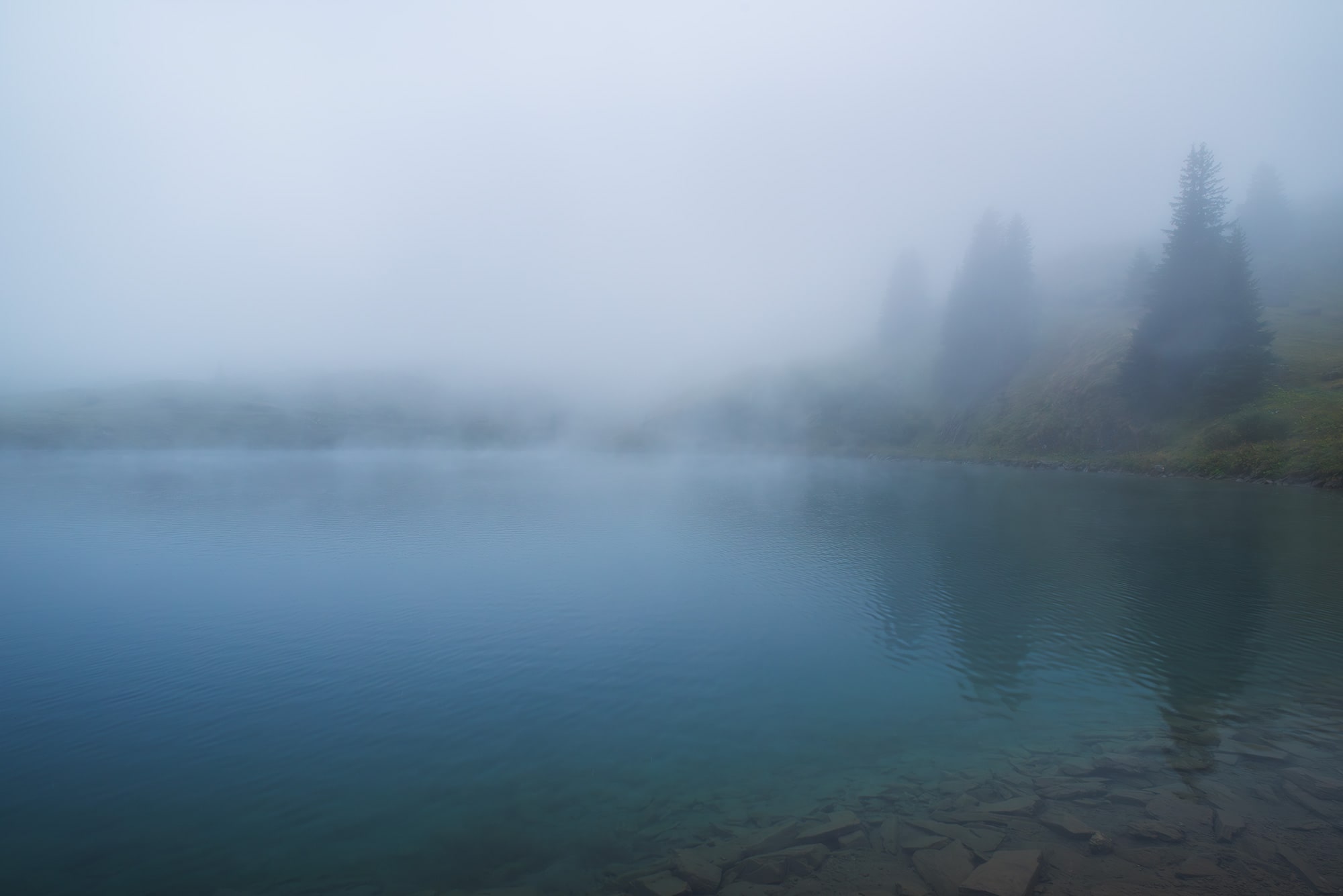Landscape photography at Lac de Lioson in Canton Vaud, Switzerland. Moody alpine lake surrounded by mountains, captured in atmospheric weather conditions.