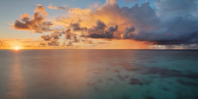 Landscape photograph capturing a romantic and paradisiac sunset in the Maldives, taken on the island of Thudufushi, showcasing vibrant hues painting the sky and reflecting off the tranquil waters.