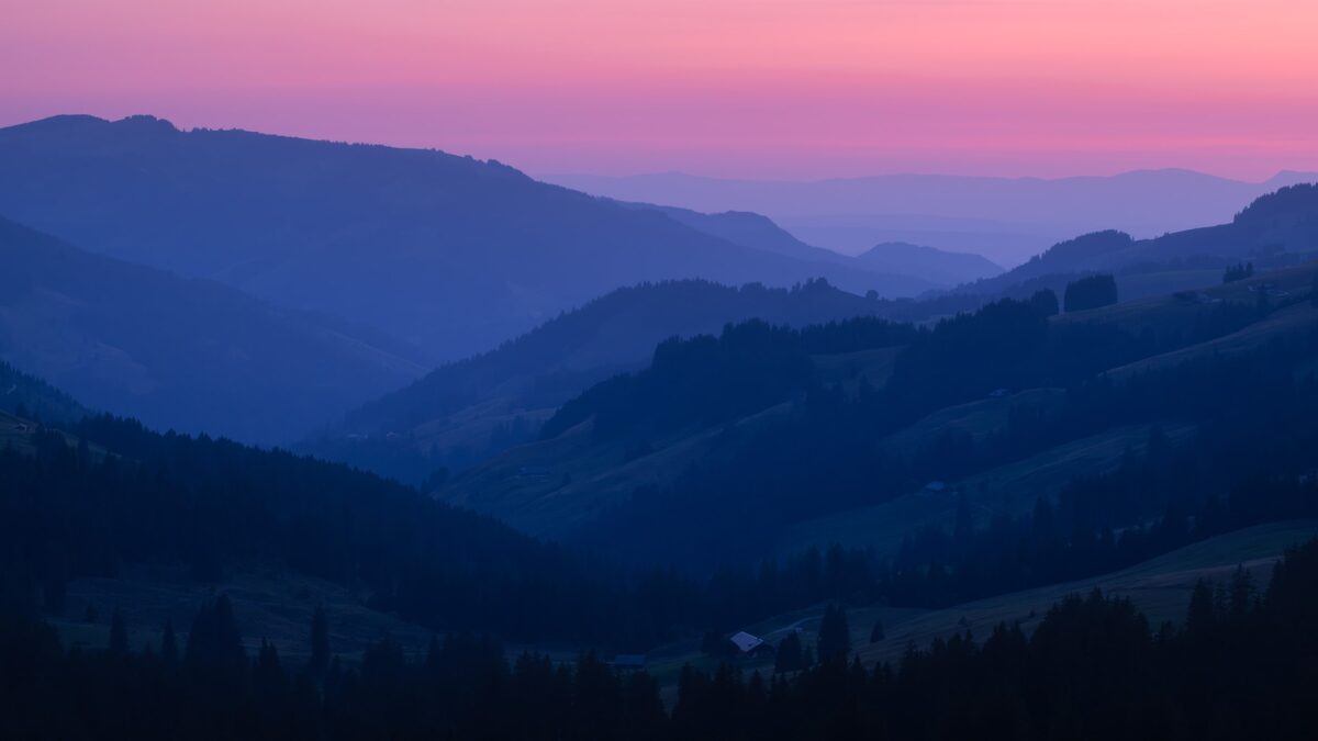 Landscape photography at twilight capturing the rolling hills of the Gantrisch Nature Park with the snowy peaks of the Bernese Oberland in Switzerland under a soft evening sky.
